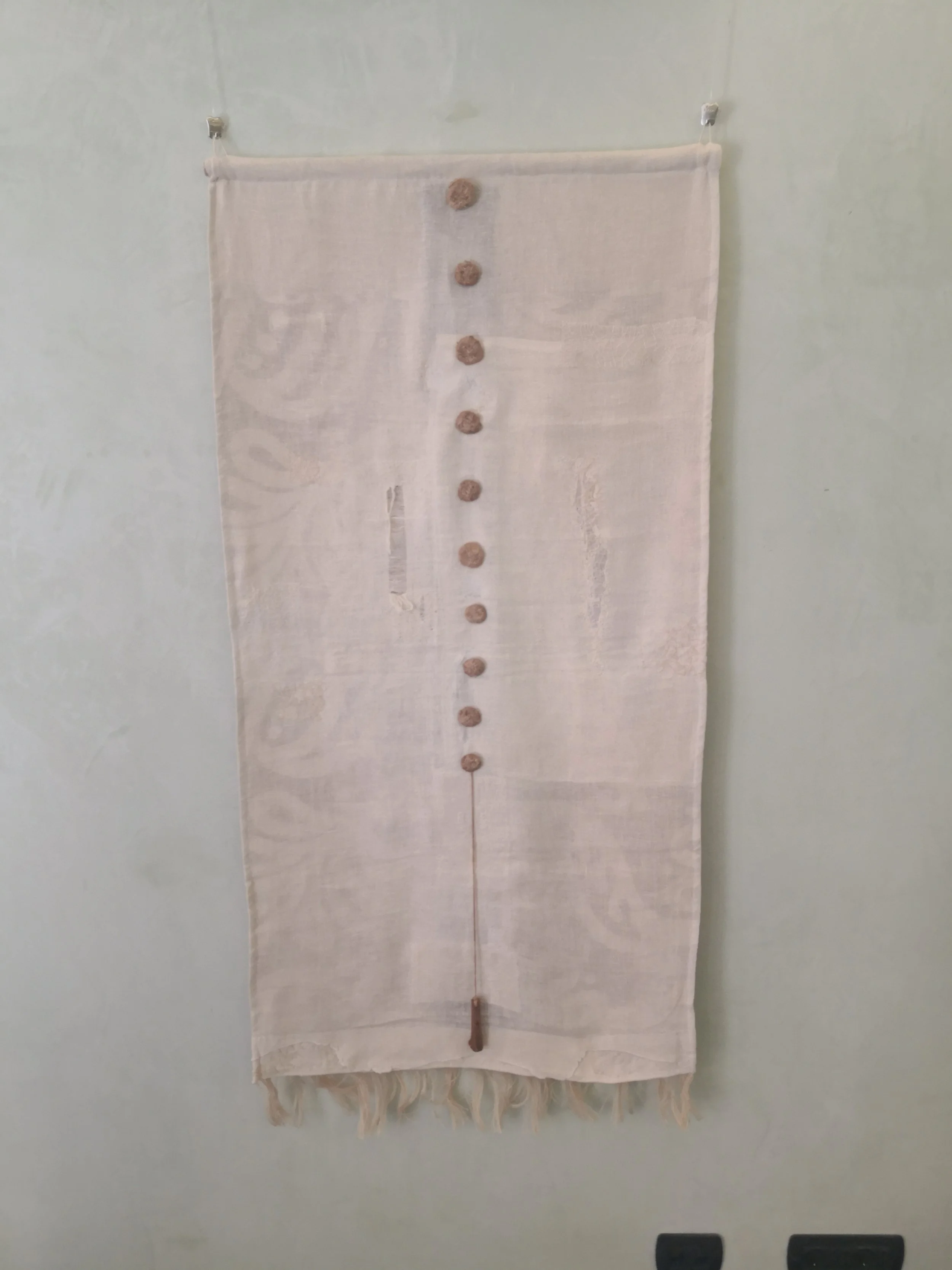 Tenda di tessuto bianco con bottoni marroni e un'asticella di legno appesa alla parete