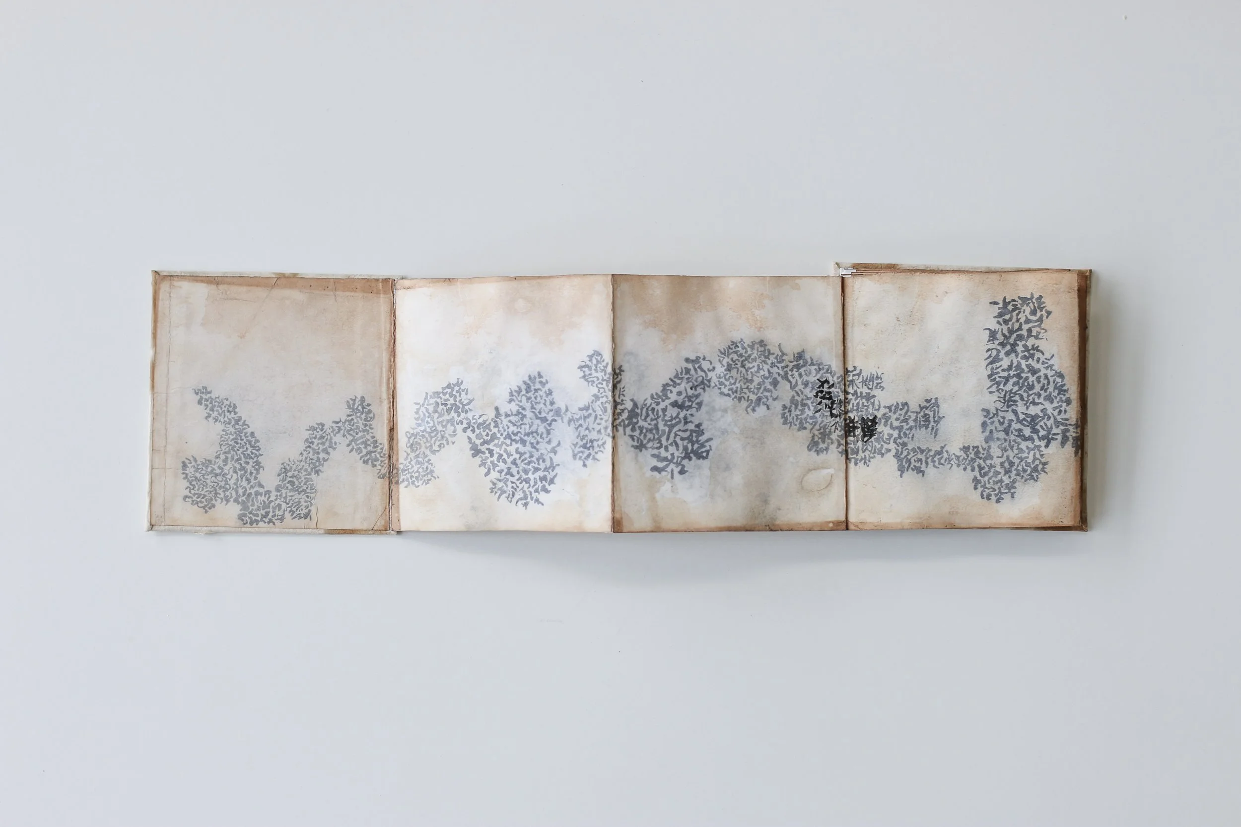 Un ventaglio aperto con un disegno di foglie stilizzate grigie su uno sfondo di carta marrone chiaro.