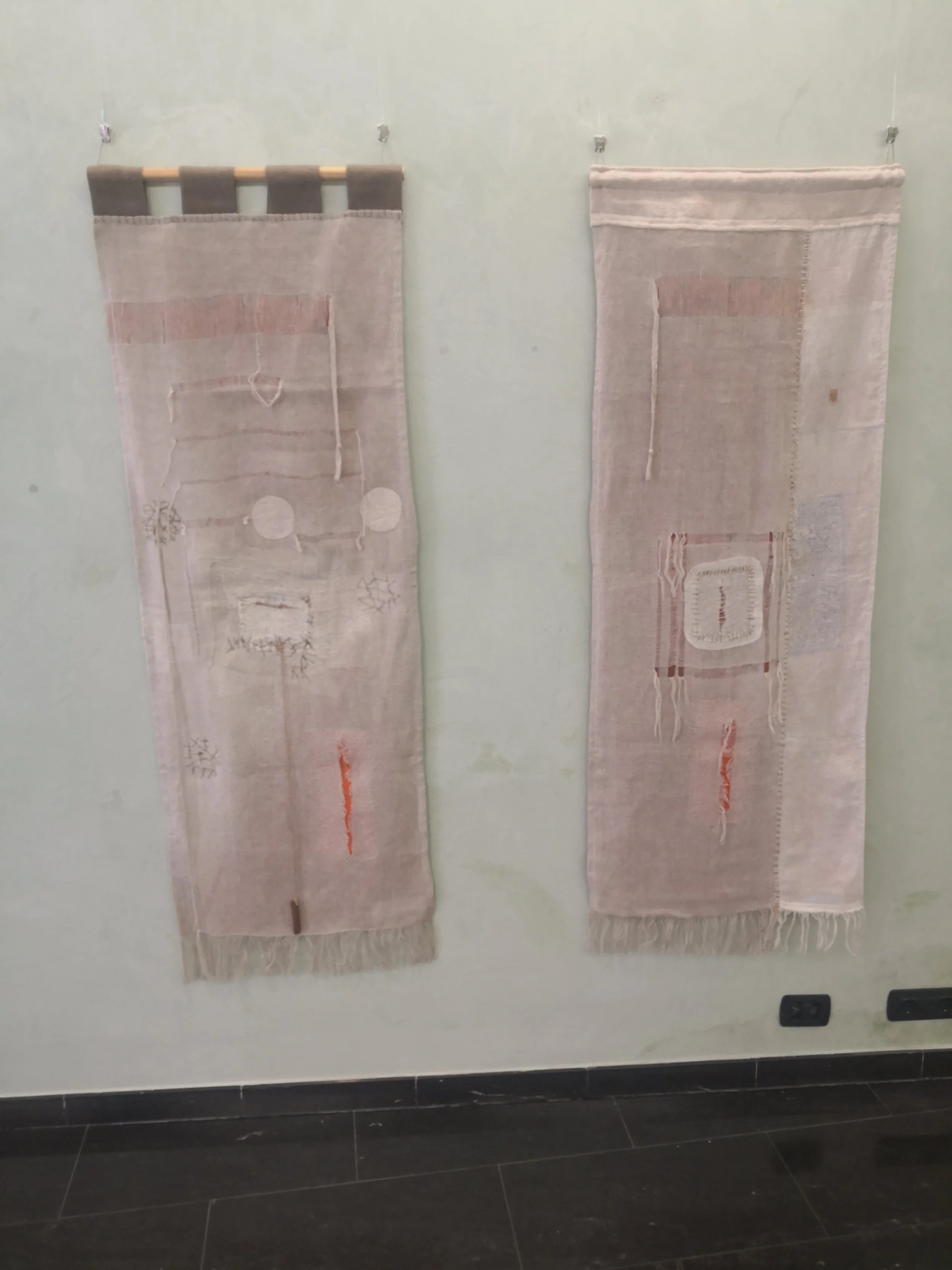 Due tapeti decorativi appesi su una parete, uno con un raggio di colori chiari e l'altro con motivi astratti e linee.