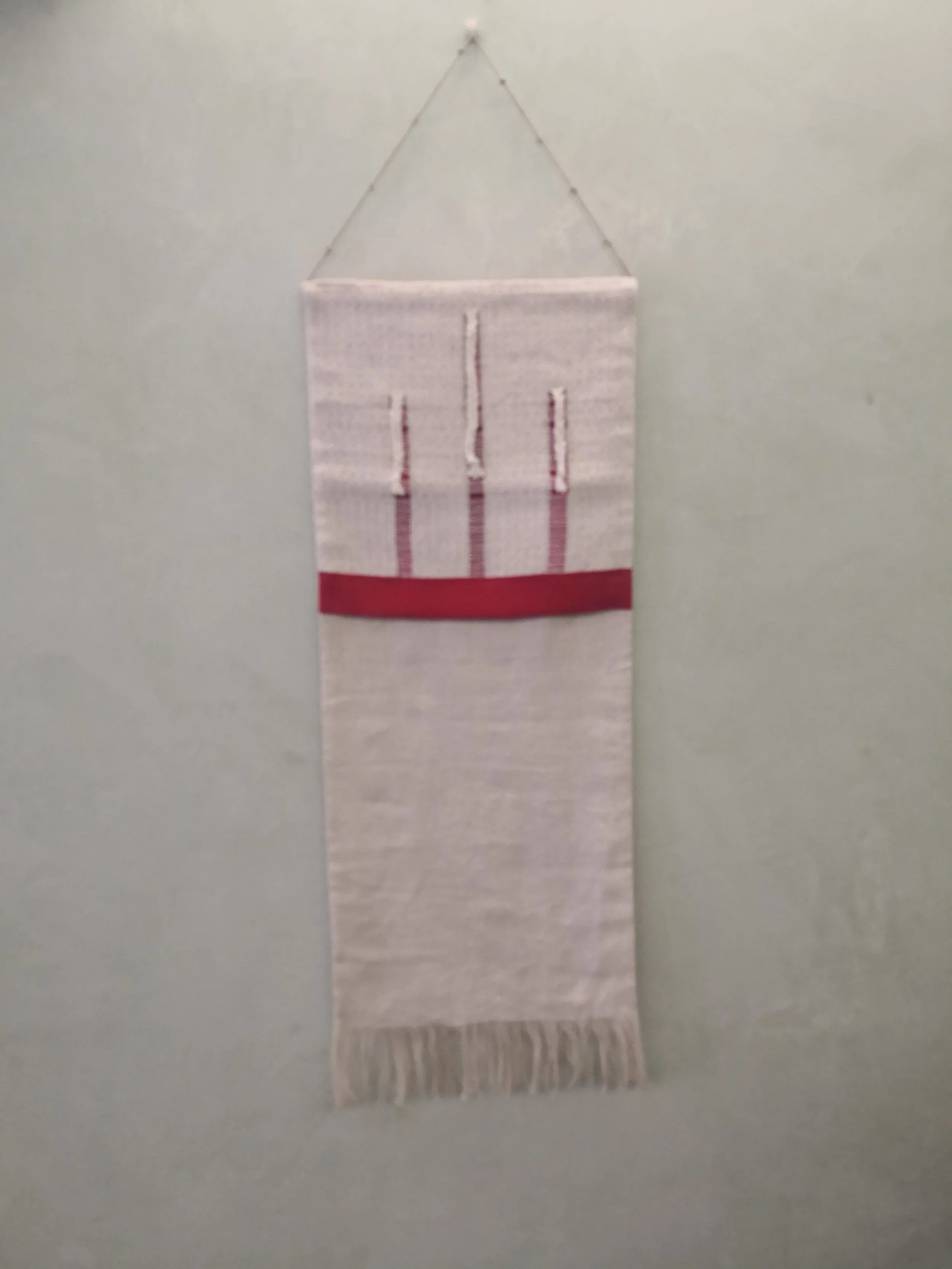 Arazzo bianco con cinque candele disegnate in alto, una banda rossa e frange in basso, appeso alla parete con un gancio.