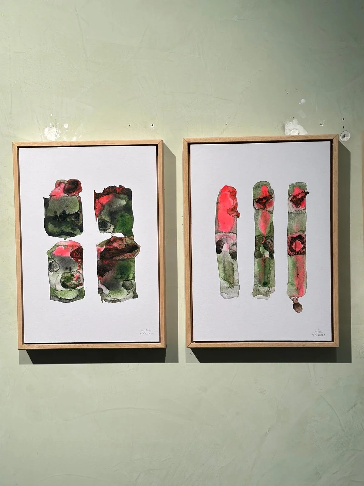 Due quadri astratti con forme rettangolari colorate di rosso, verde e nero, appesi su una parete verde chiaro.