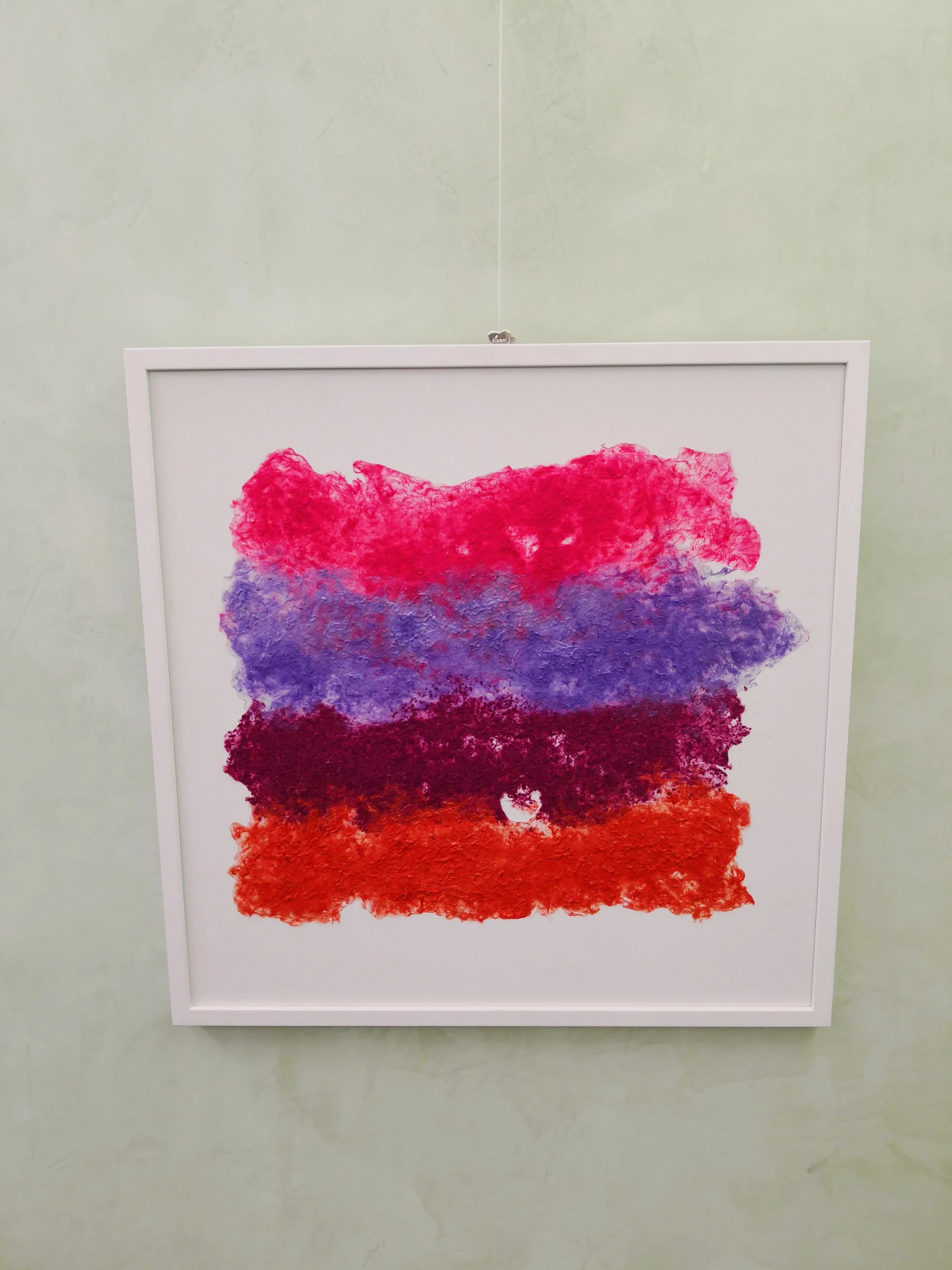 Un quadro astratto con strati di colori rossi, viola e blu in una cornice bianca.