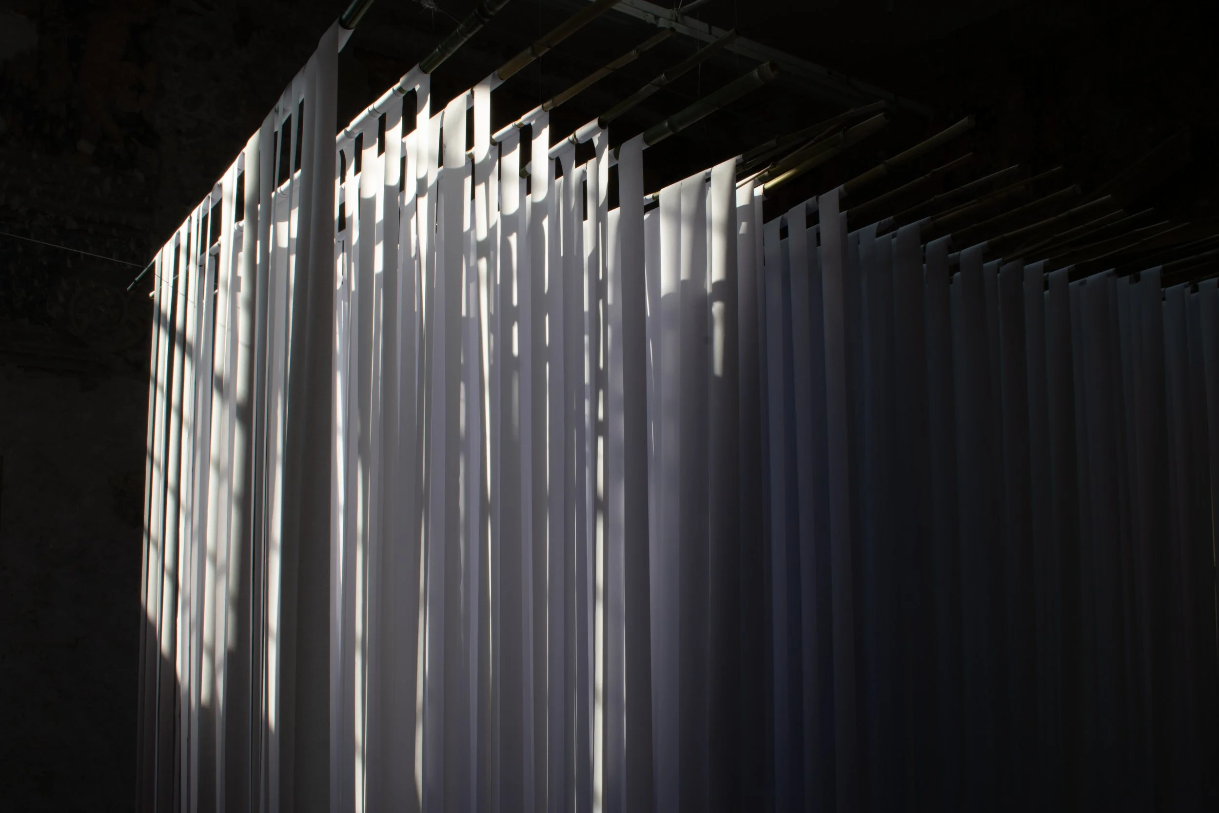 Strisce di tessuto bianco sospese in un ambiente buio con luci che creano ombre.