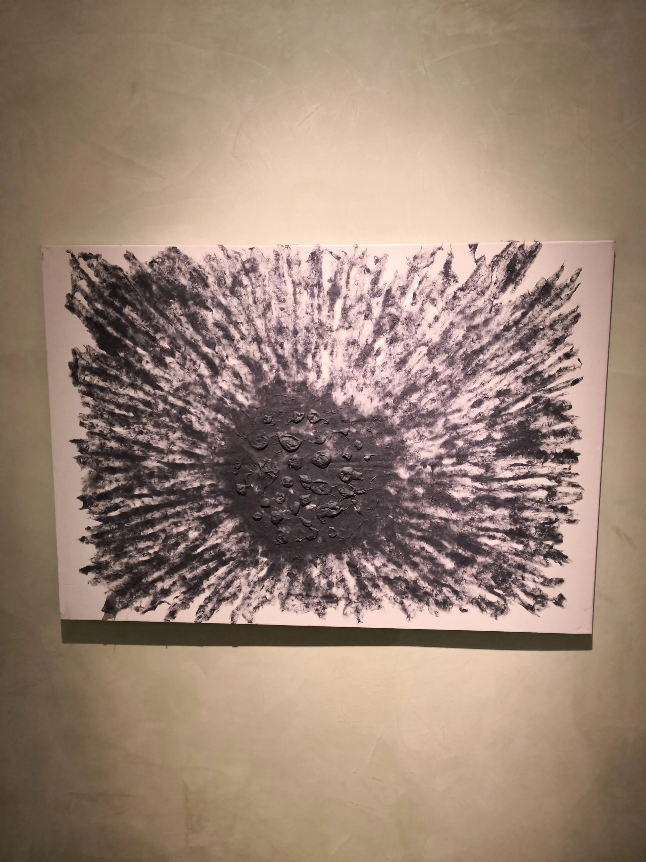 Un dipinto astratto con una raggiera di linee nere che partono da un centro scuro, con al centro alcune rocce o elementi di pietra di colore grigio