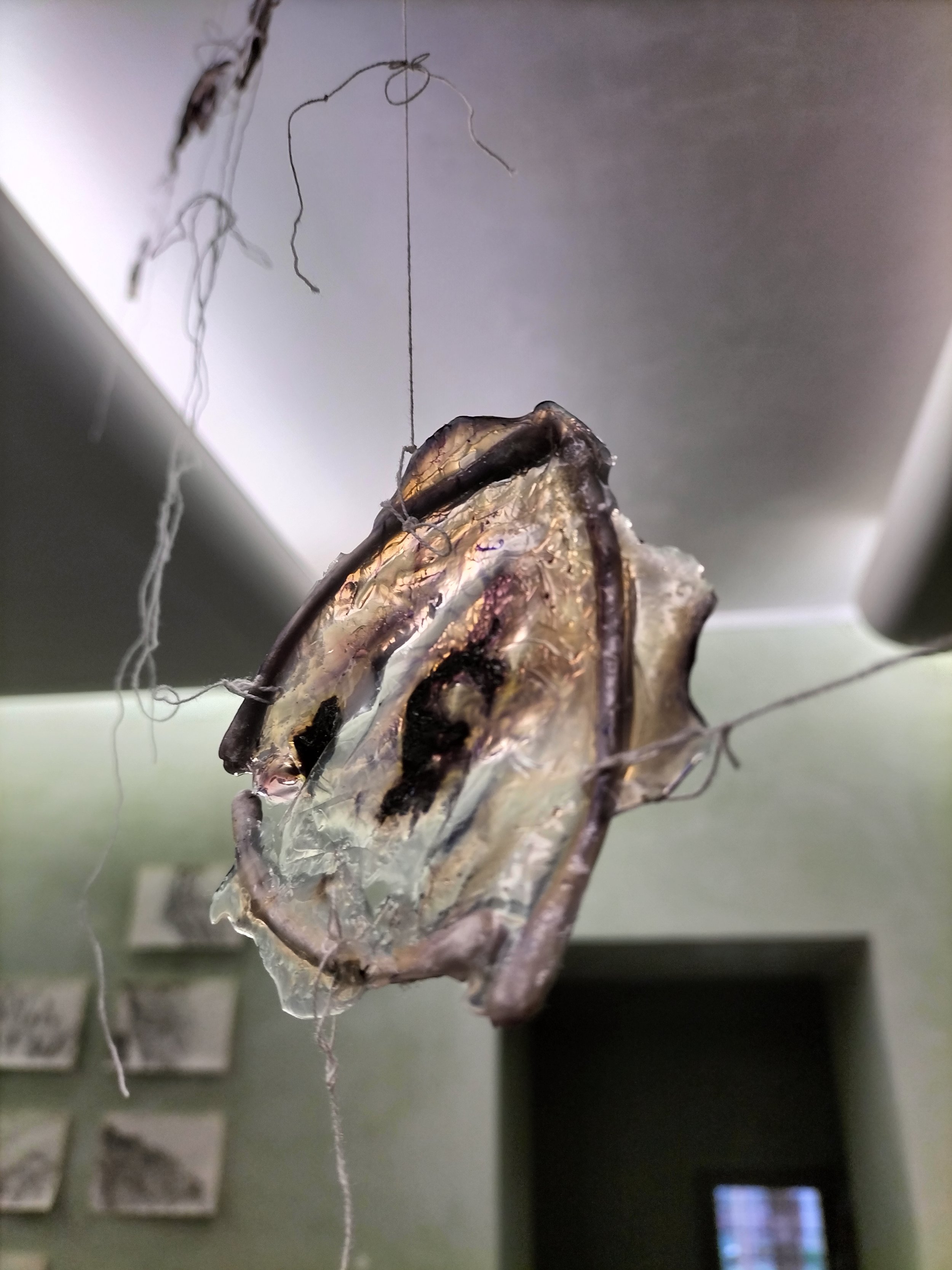 Un'installazione artistica con un oggetto appeso al soffitto, composto da vari materiali e fili che lo tengono sospeso.