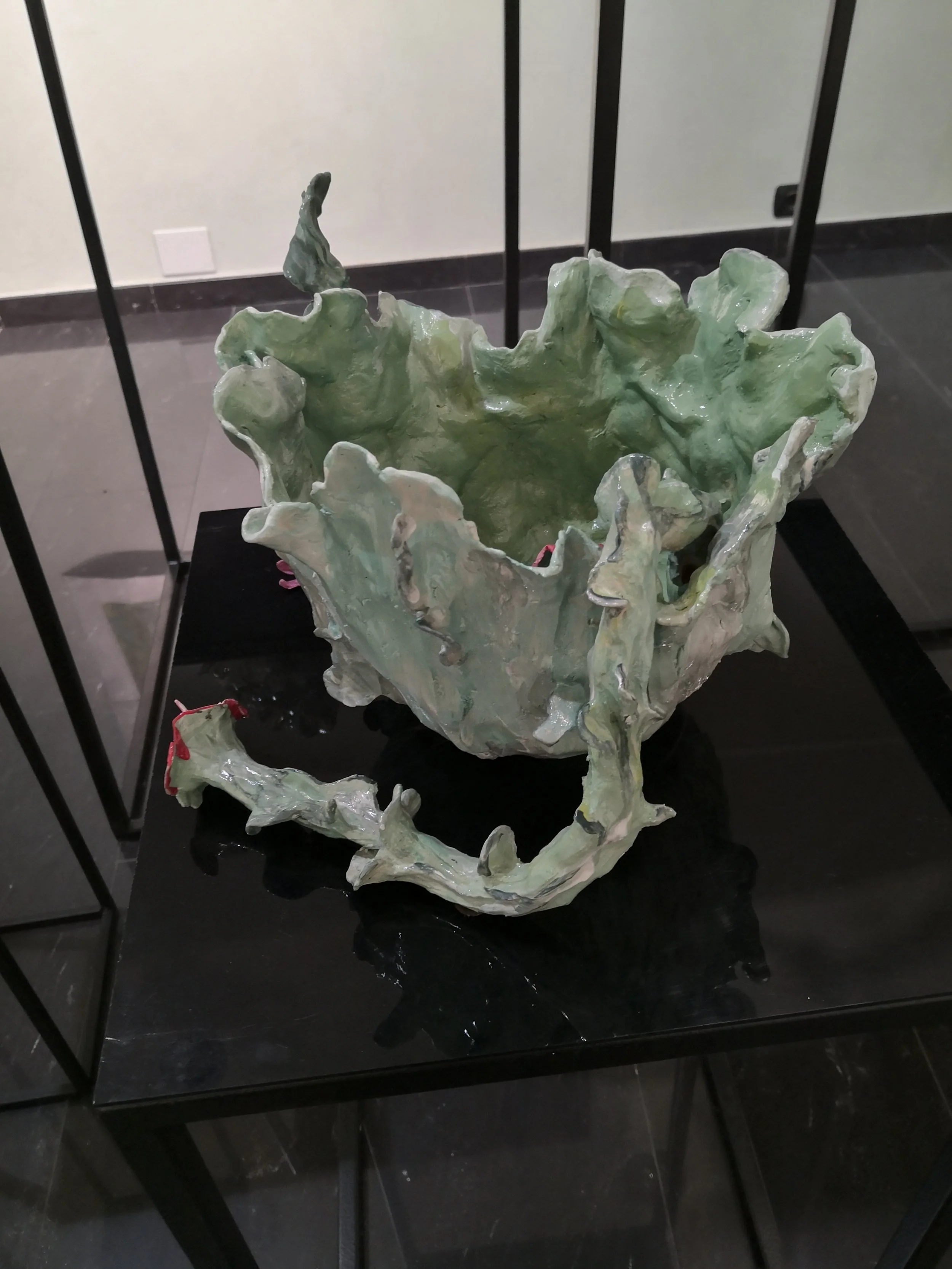 Scultura in ceramica con forma organica, di colore verde, esposta su una piattaforma nera in un museo.