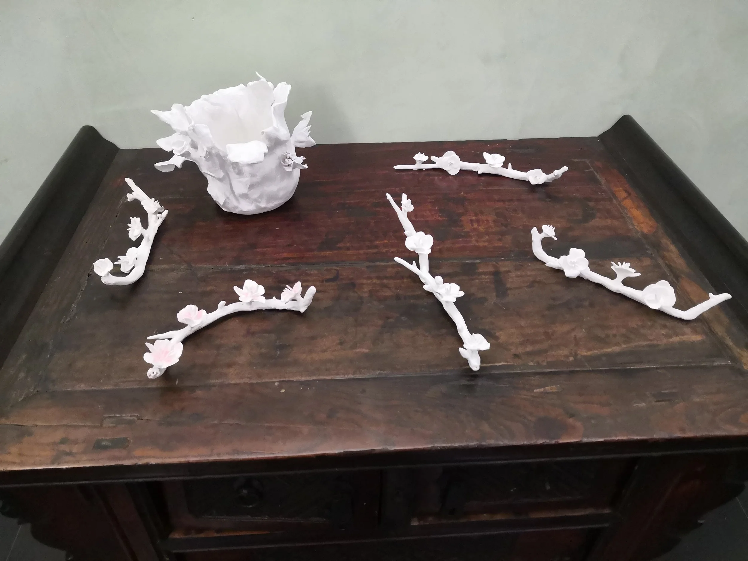 Piccoli capolavori di arte con elementi di plastilina bianca, alcuni a forma di rami con fiori, collocati su un tavolo di legno antico.