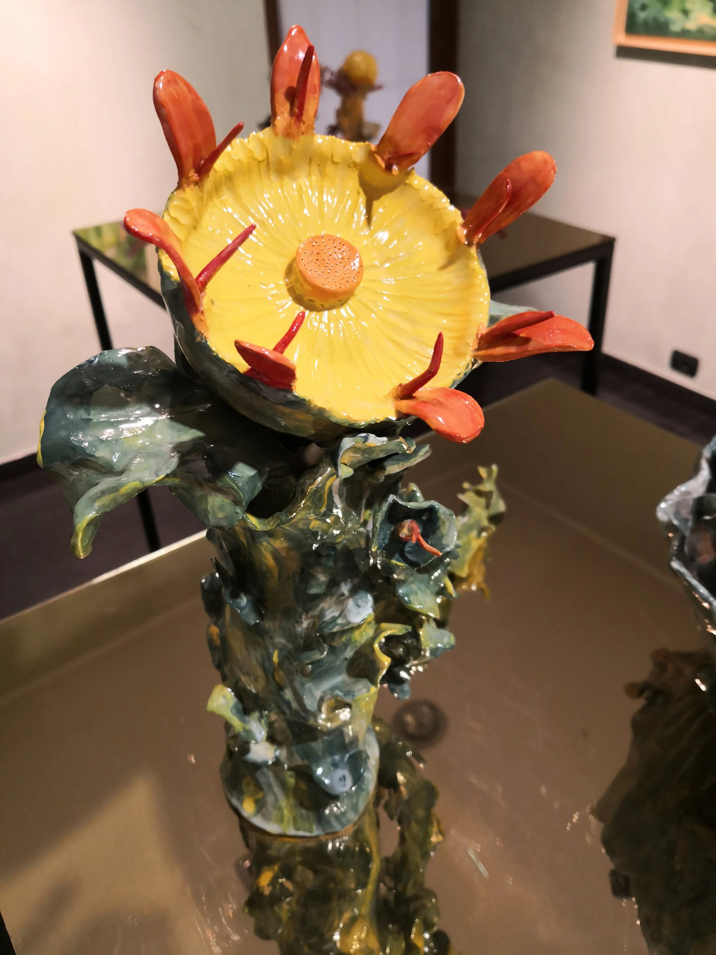 Scultura artistica di un fiore con petali rossi e centro giallo, realizzata in ceramica o materiale simile.
