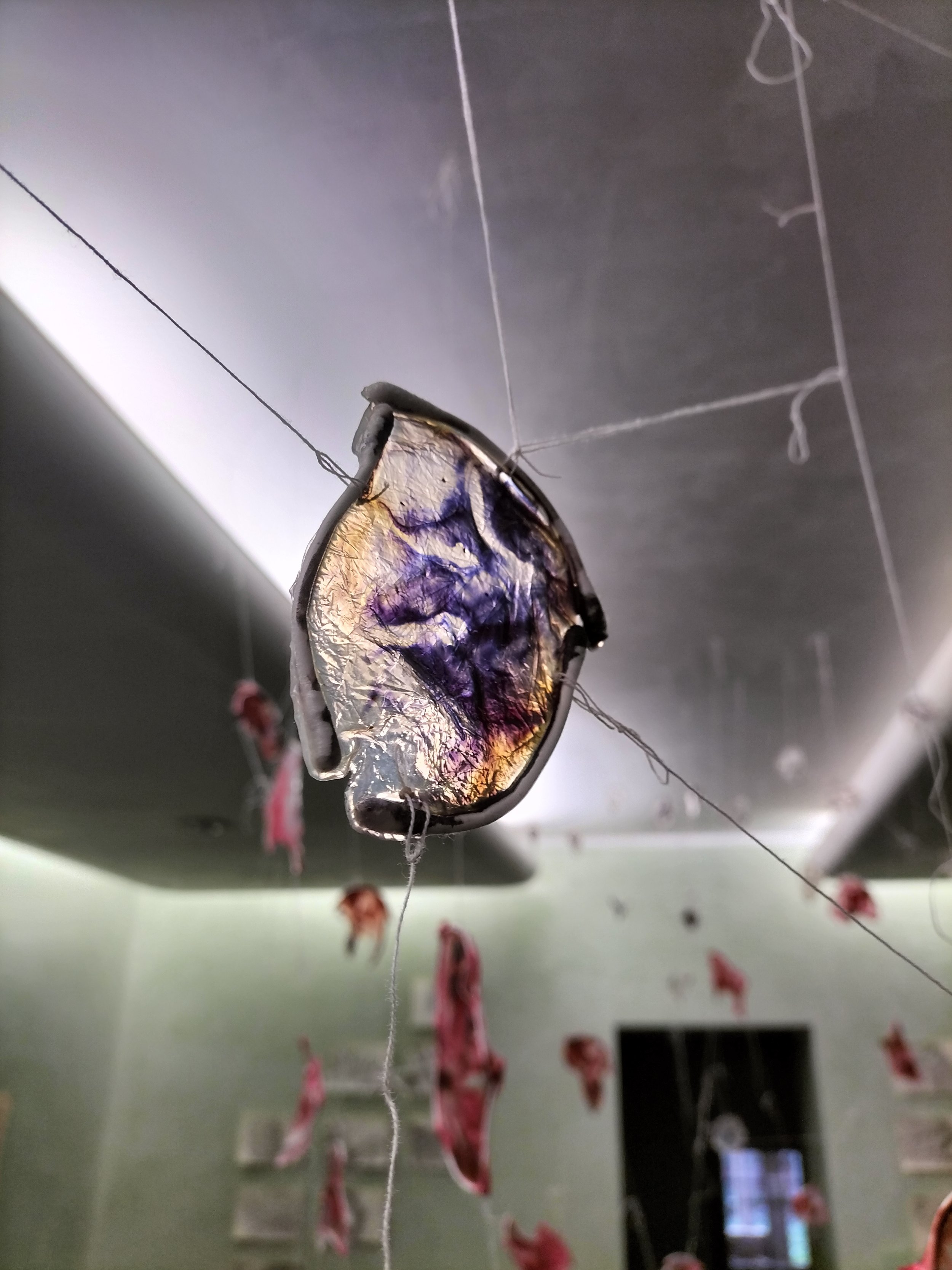 Oggetto appeso al soffitto, simile a una pietra o un vetro iridescente, circondato da fili