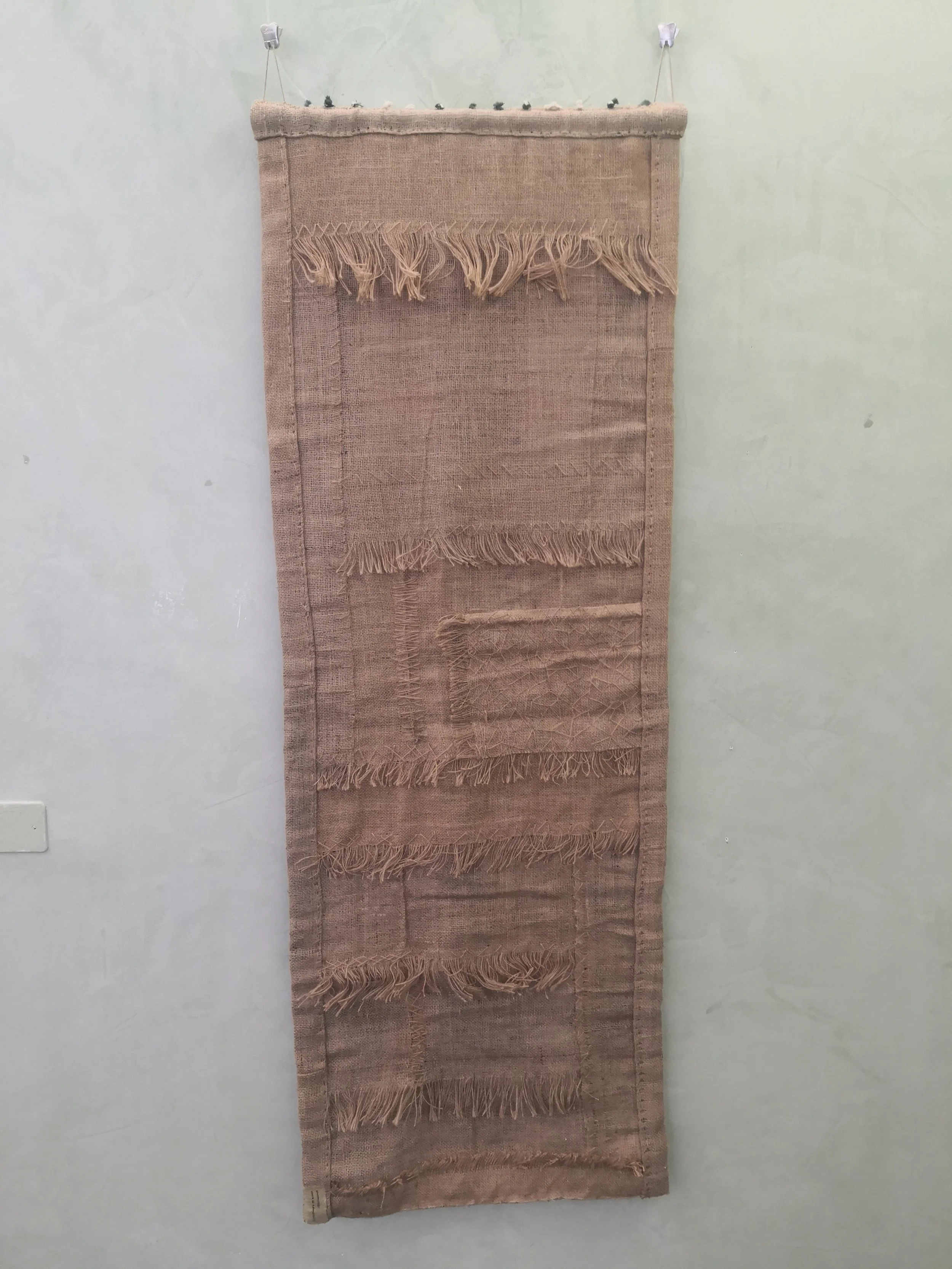 Tappeto lungo color pesca con frange e vari motivi tessuti, appeso su una parete