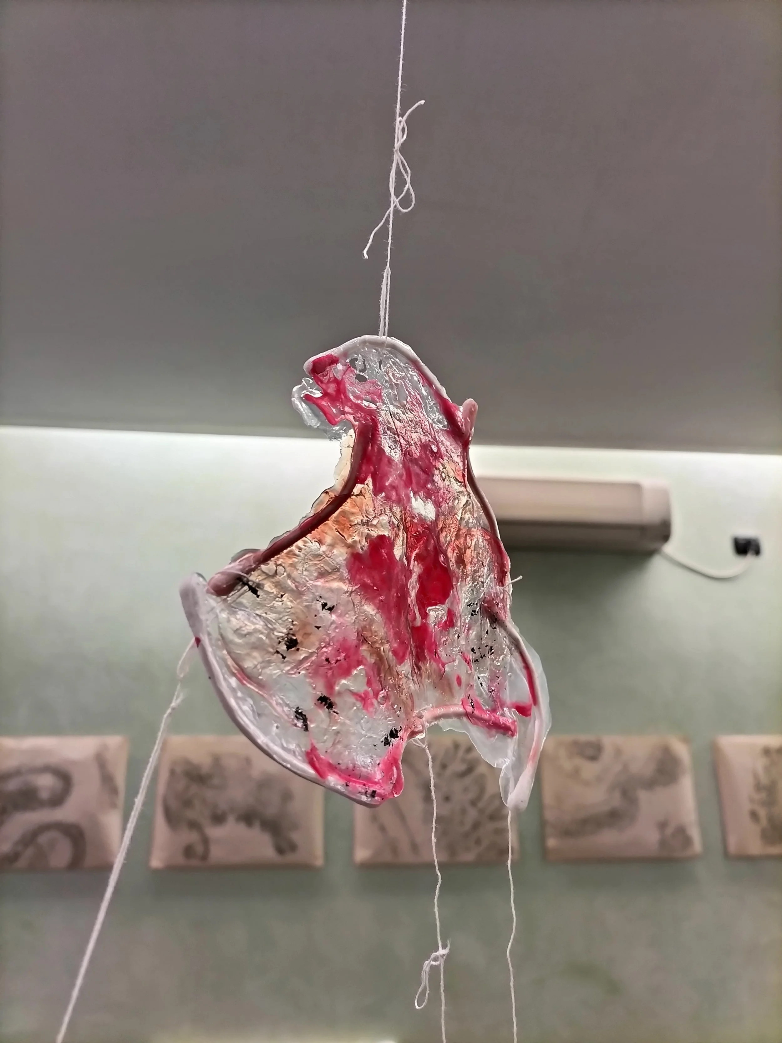 Onda di vetro colorato incrociata con fili di filo bianco sospesi in aria, con un muro verde chiaro e quadri sullo sfondo.