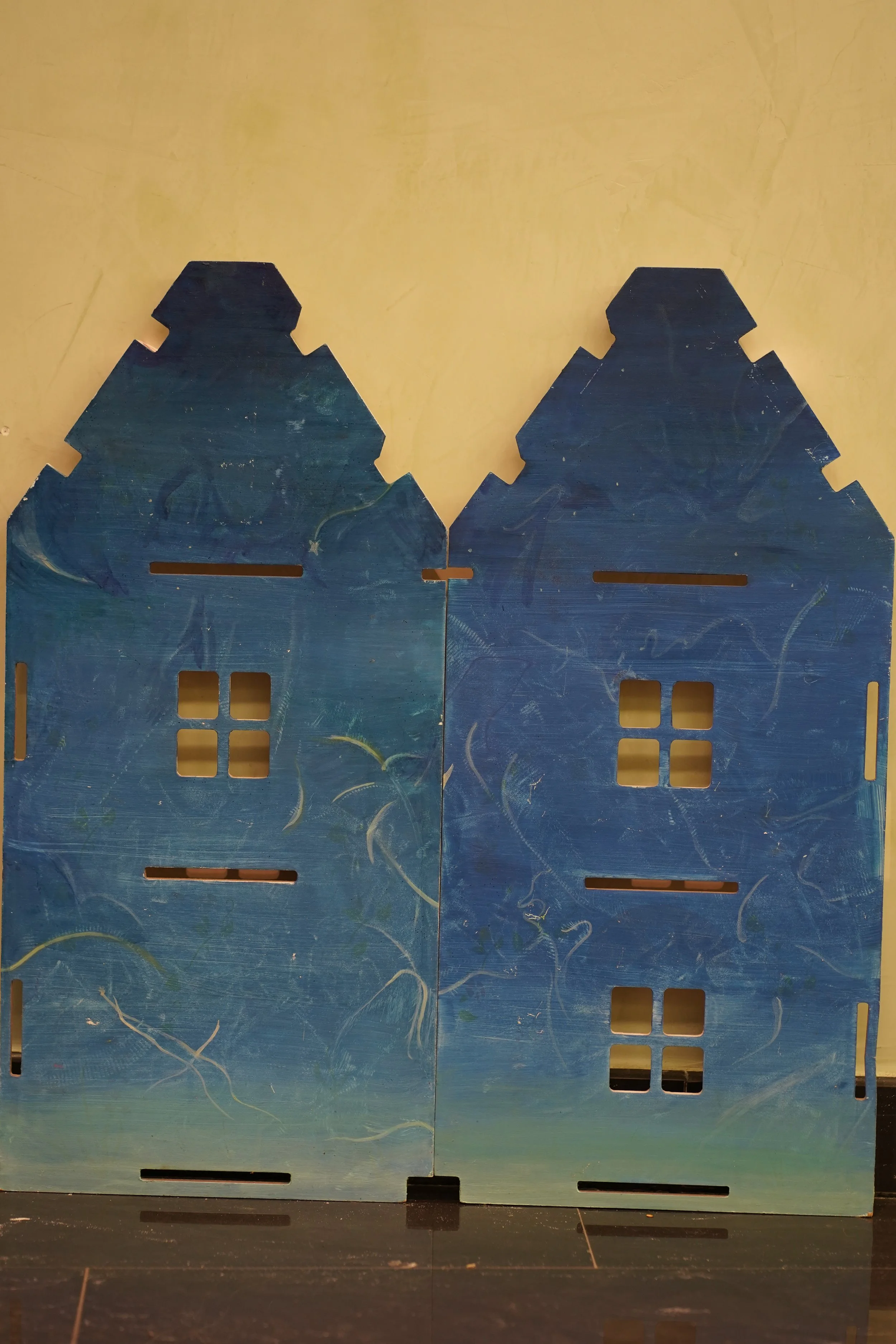 Due casette di legno blu con tetti a forma di casa, posizionate vicine, sul pavimento.