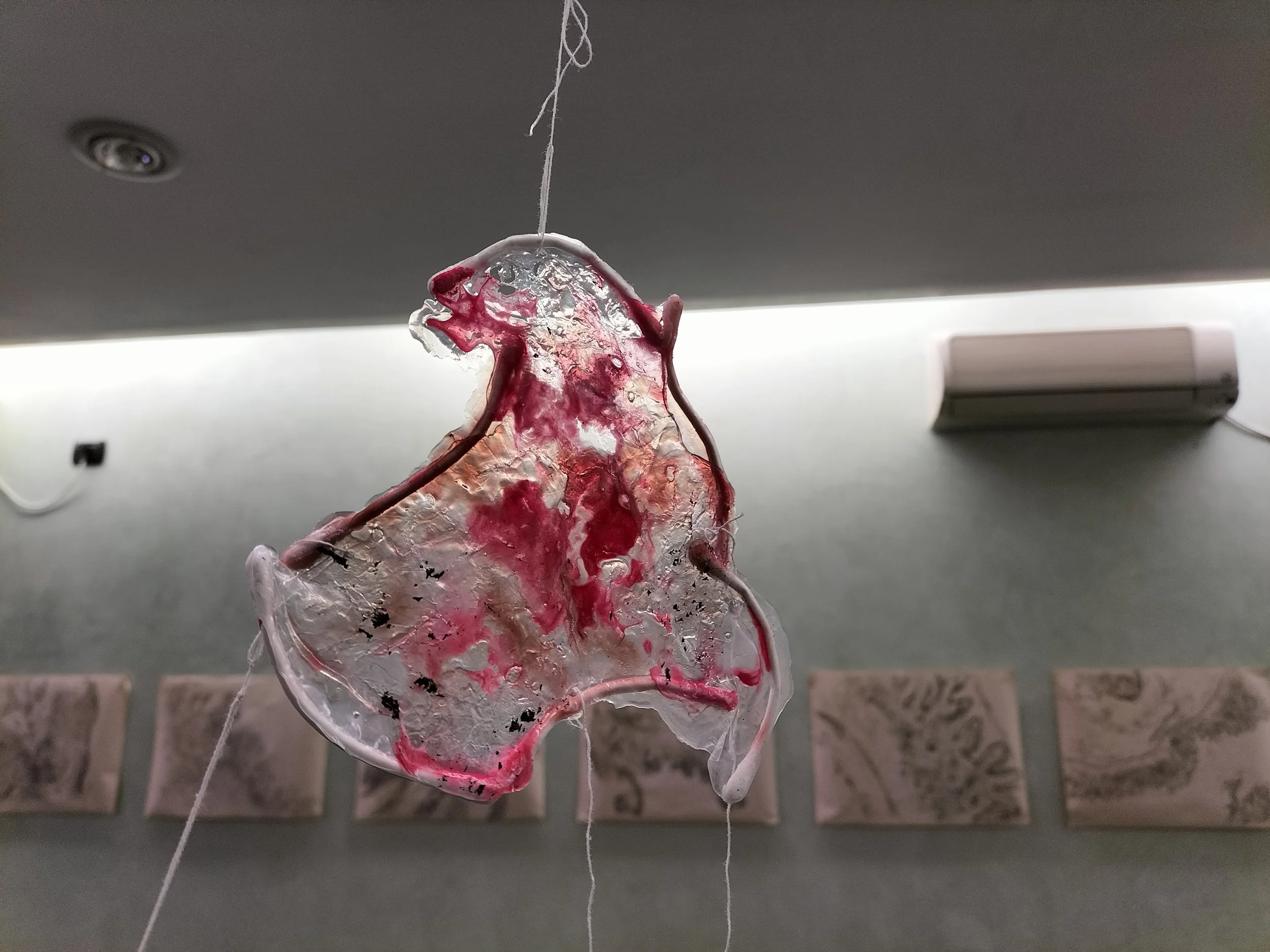 Decorazione di vetro trasparente con motivi rossi, appesa con fili in ambienti interni con pareti con quadri e aria condizionata.