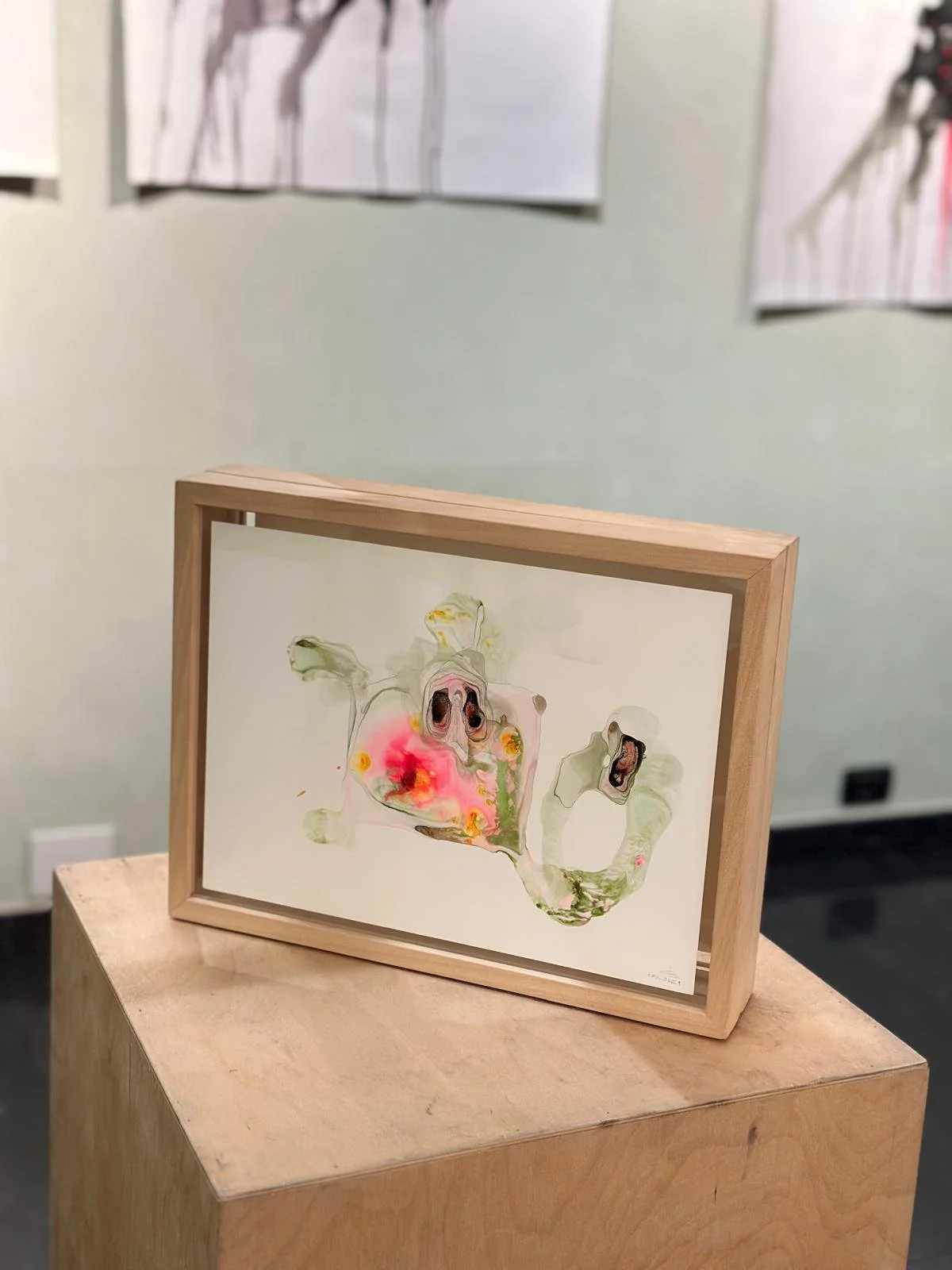 Opera d'arte astratta su carta all'interno di una cornice di legno, collocata su un supporto di legno in una galleria