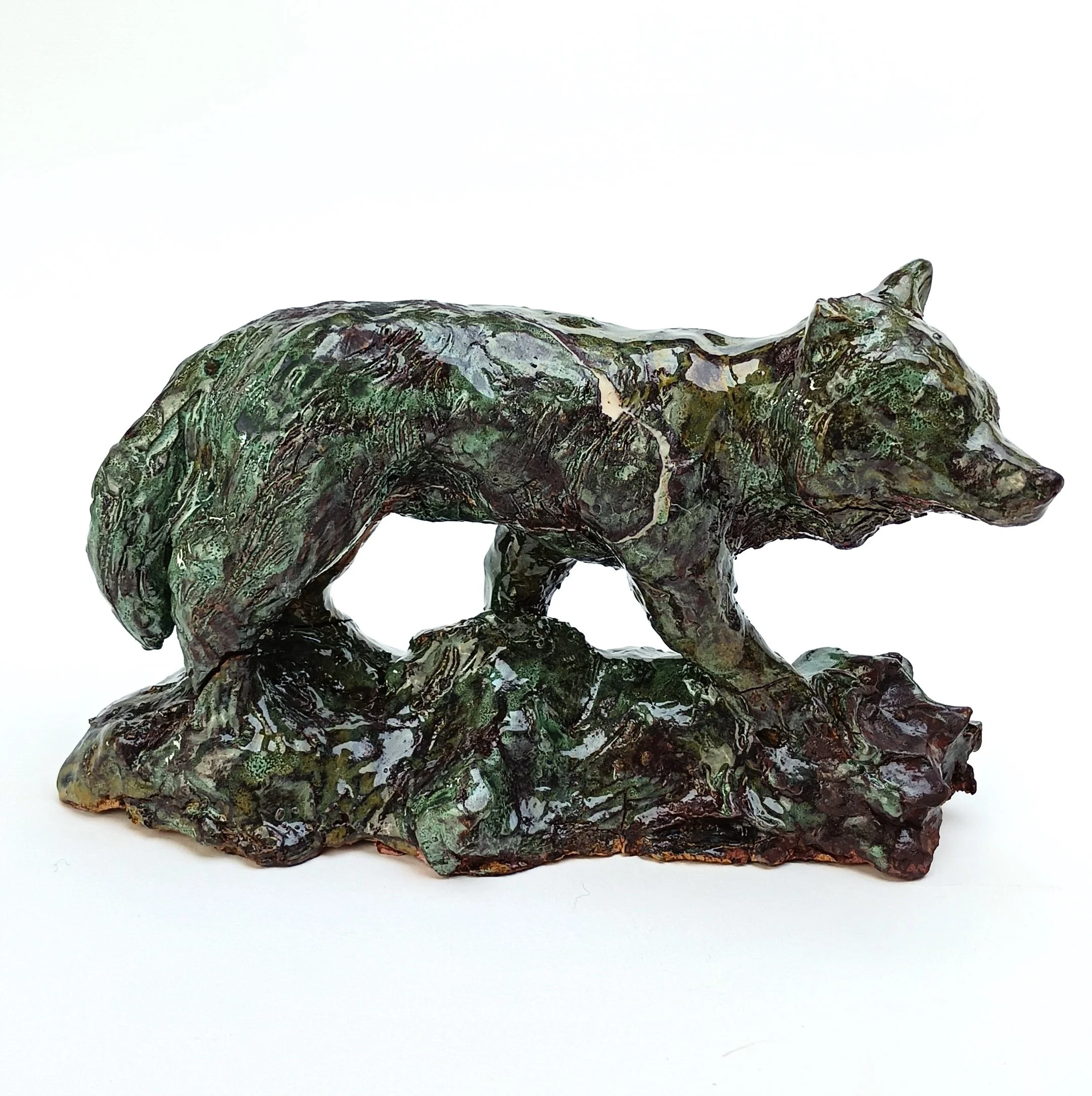 Statua di un lupo in pietra con finiture verdi, posizionato su una roccia, sfondo bianco.