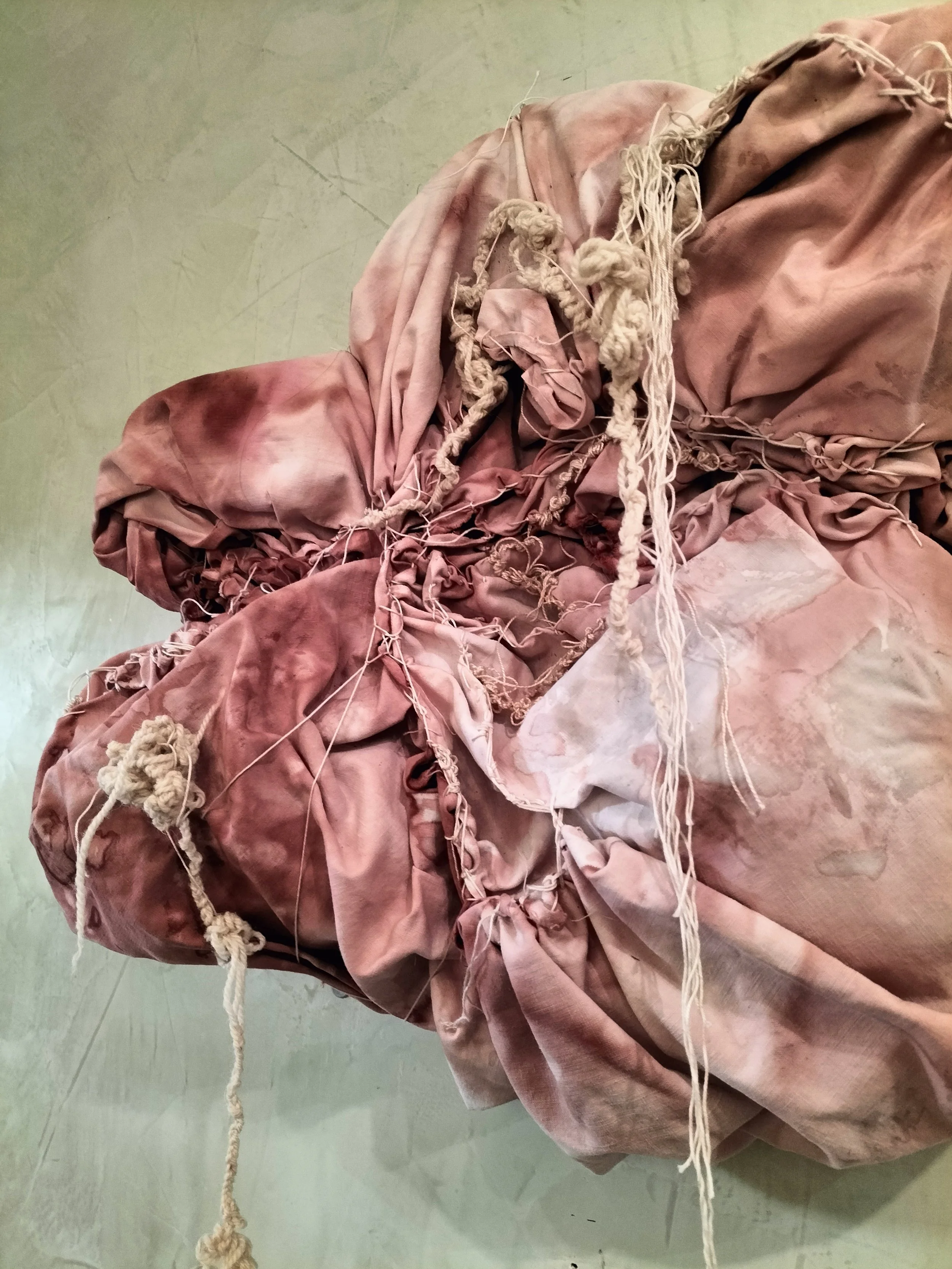 Un ammasso di tessuto rosa sporco e rovinato, con pezzi di corde annodate e arricciate.