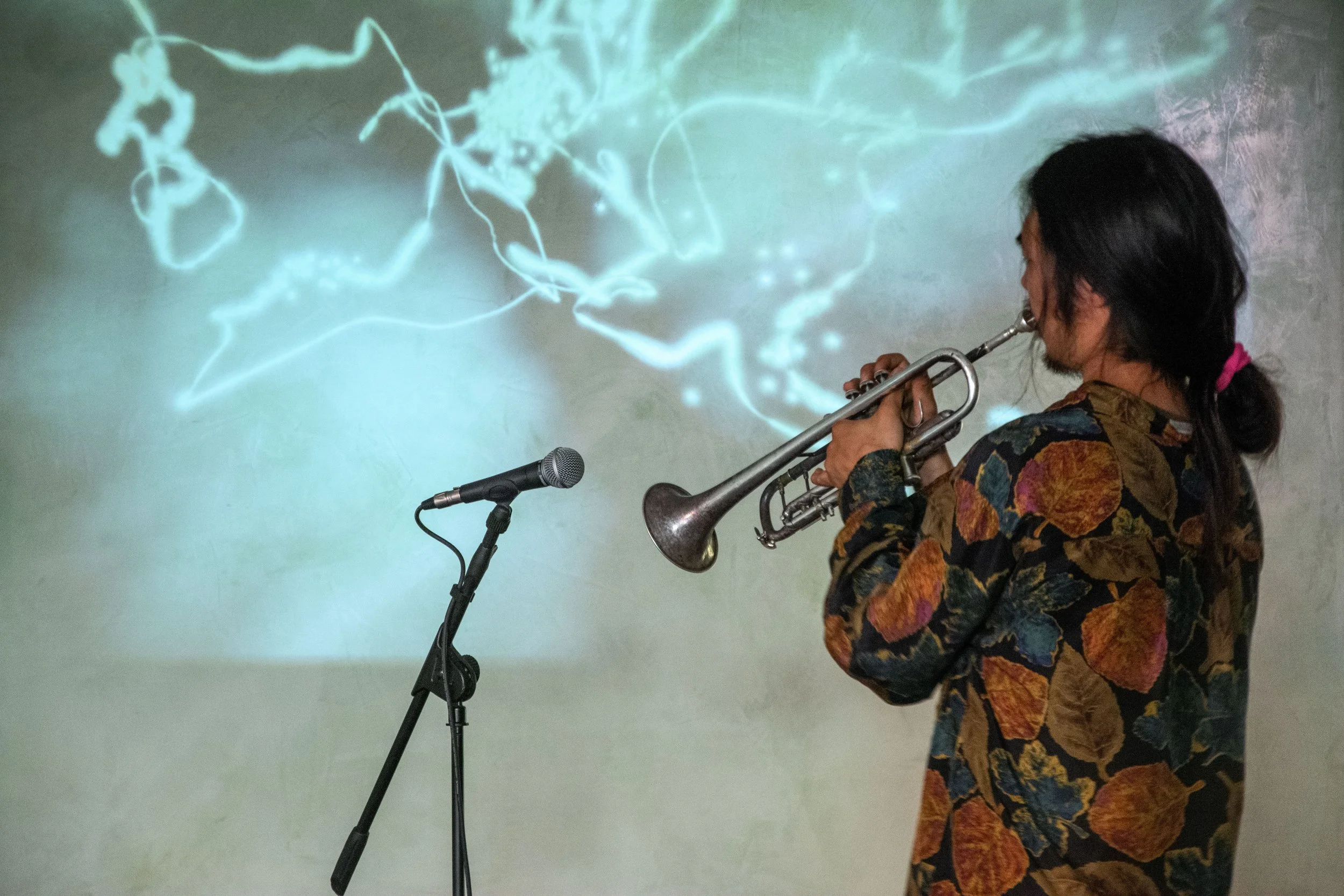 Un musicista che suona la tromba davanti a uno schermo con un'immagine di luci blu e verdi.