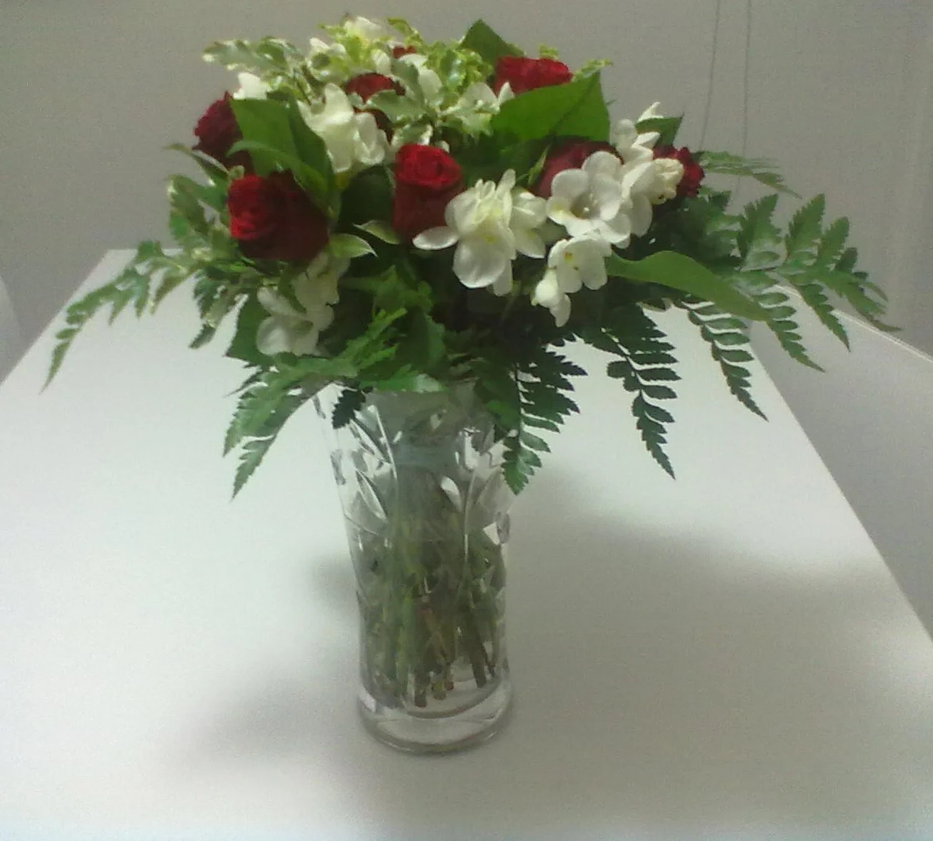 Mazzo di fiori con rose rosse, fiori bianchi e foglie verdi in un vaso di vetro trasparente.