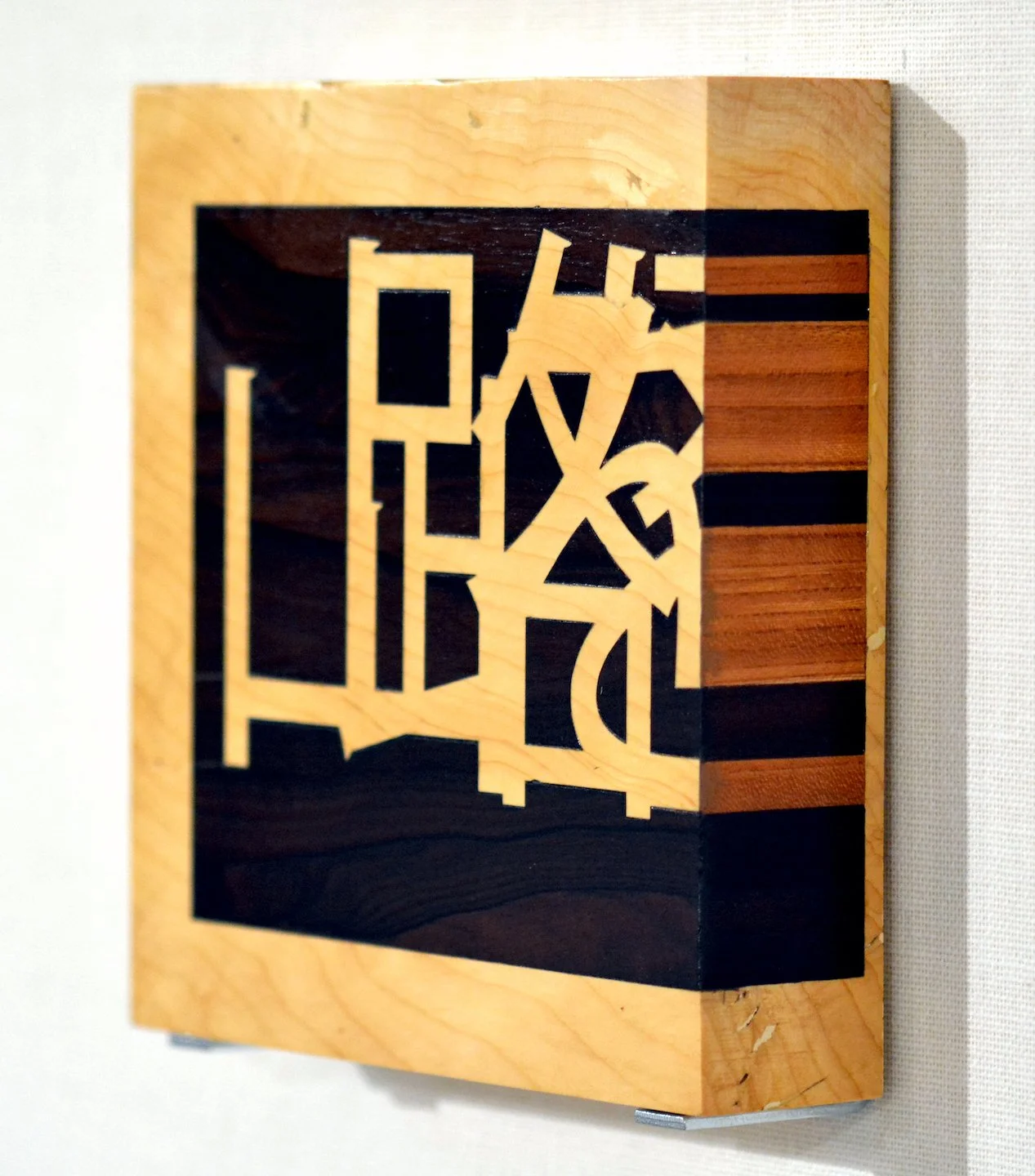 Un quadro di legno intarsiato con un design astratto, collocato su una parete bianca.