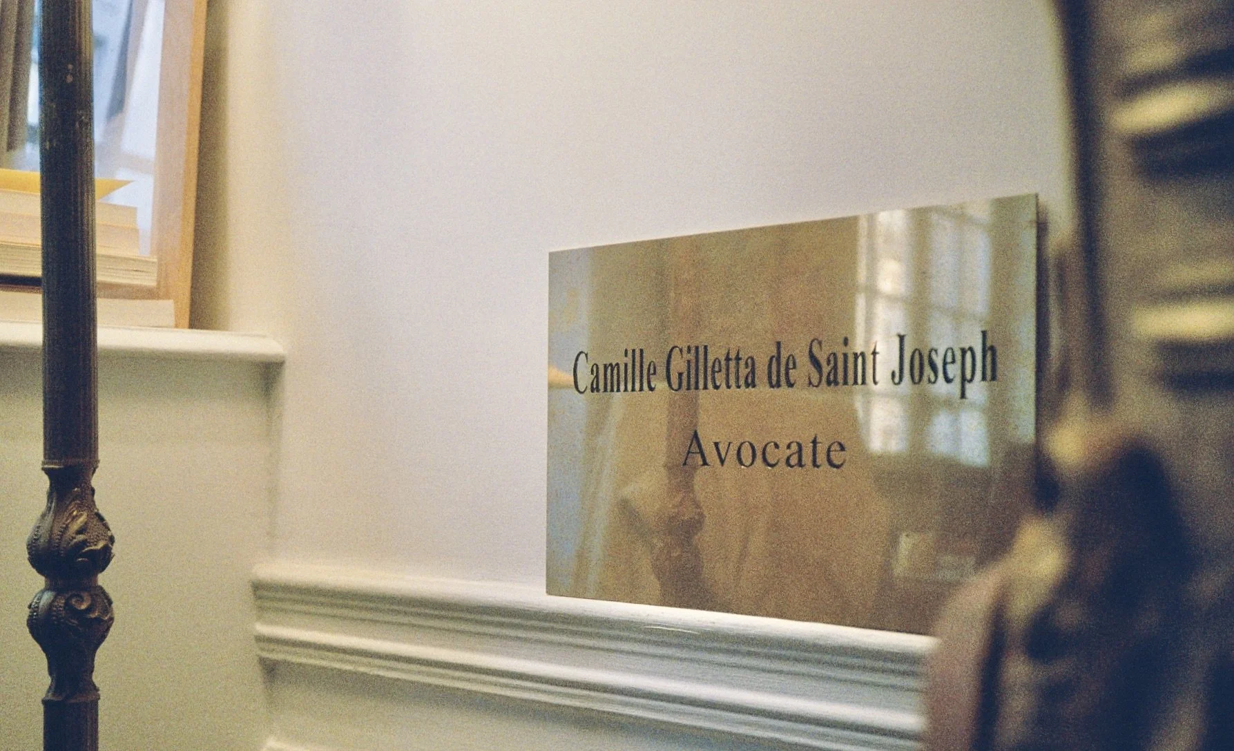 Plaque en métal indiquant le nom 'Camille Gulletta de Saint Joseph' et la profession 'Avocate', située à côté d'une rampe d'escalier en fer forgé.