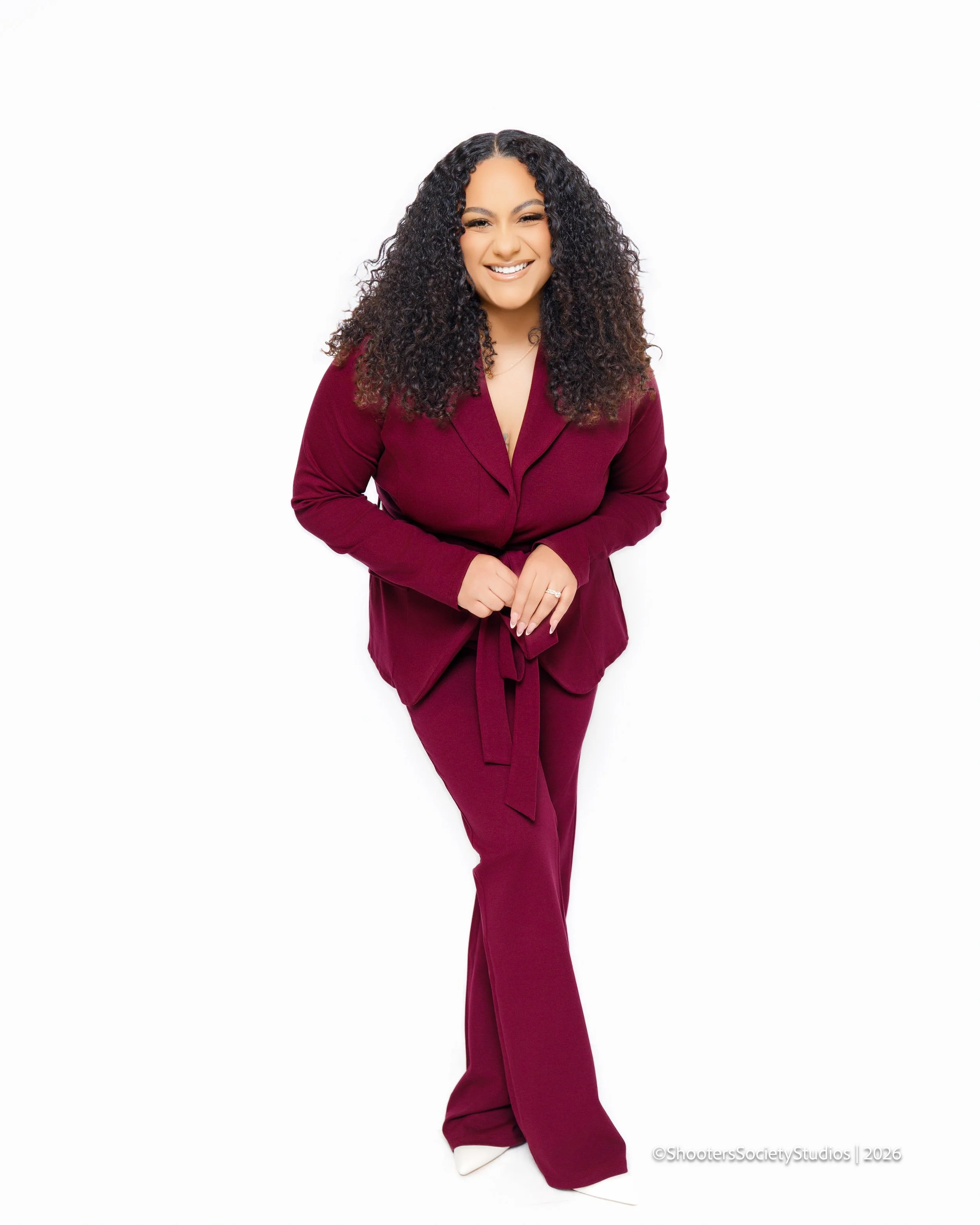 Woman with curly hair in a maroon suit smiling and leaning forward