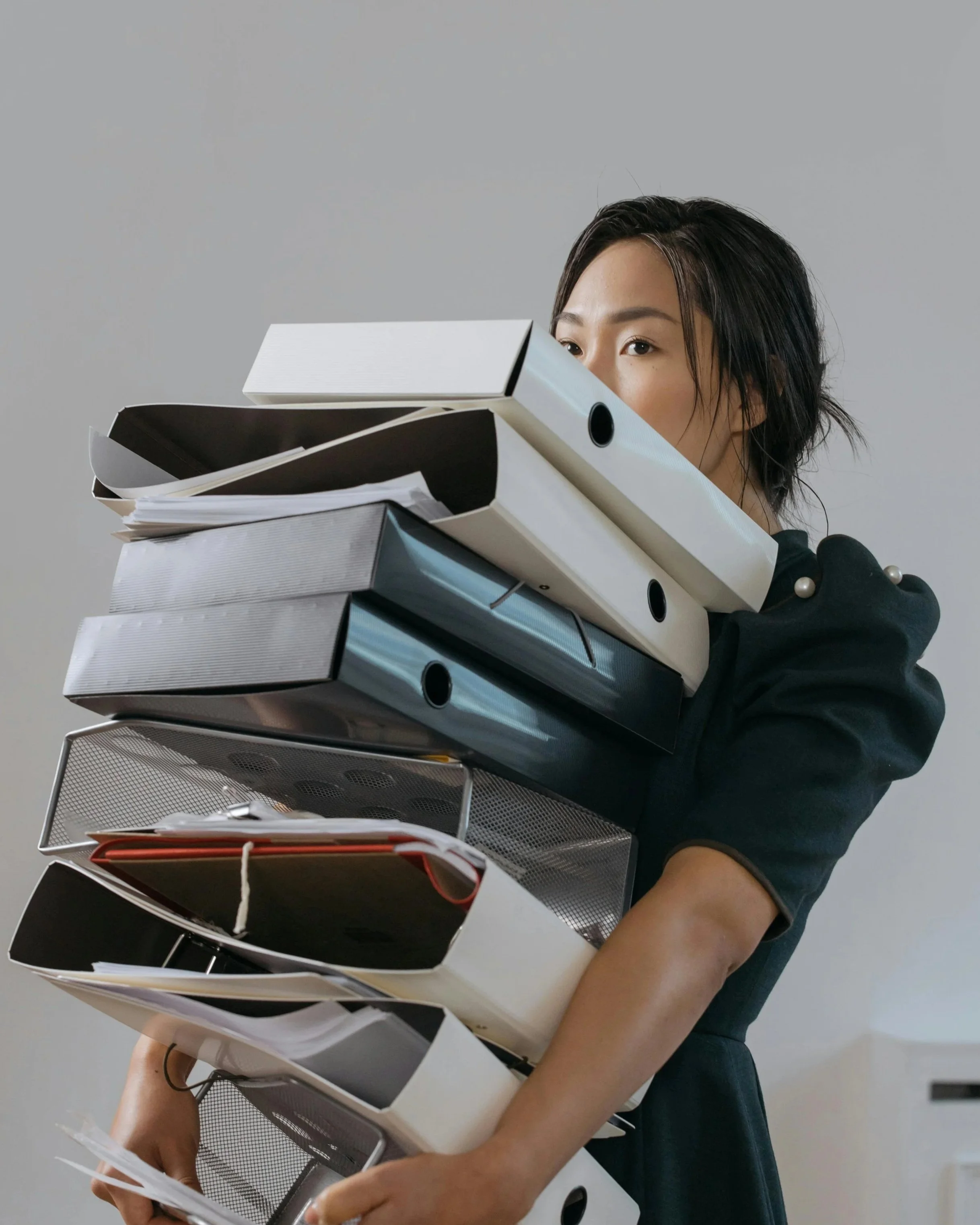 Woman holding a large stack of office binders and papers.