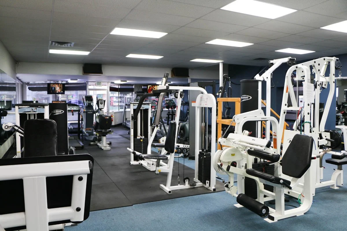 Interior of a gym with various exercise machines and weight equipment, with bright overhead lighting.