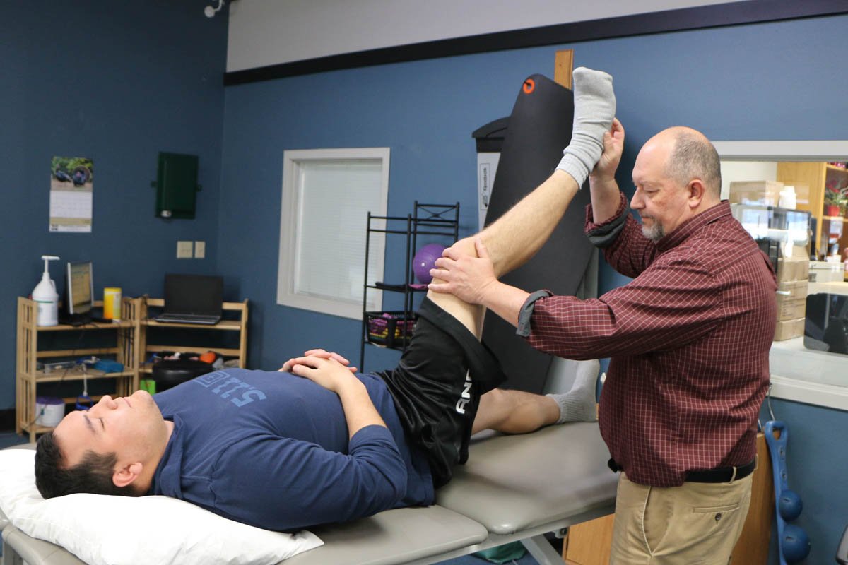 Physical therapist assisting a patient with leg exercises on a treatment table in a therapy room.