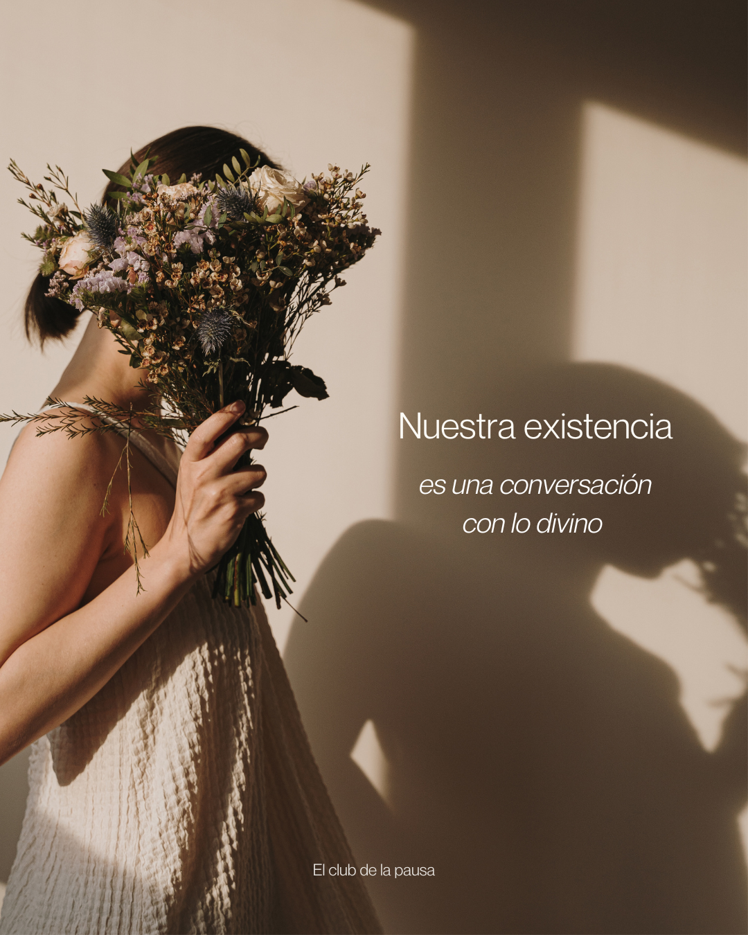 A woman holding a bouquet of flowers covering her face, with a shadow cast on the wall behind her. The scene has warm lighting and a minimalist background.