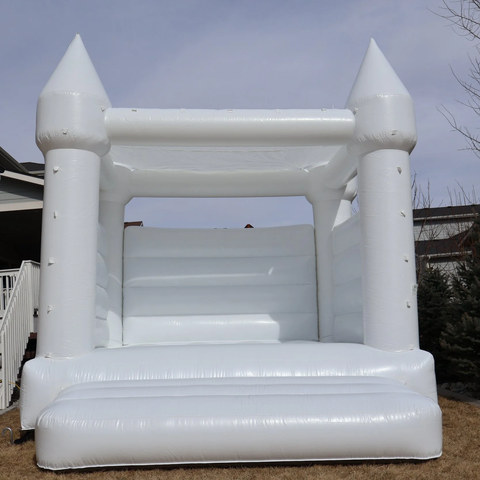 Large white inflatable bounce house in the shape of a castle with towers, set up outdoors on a grassy area.