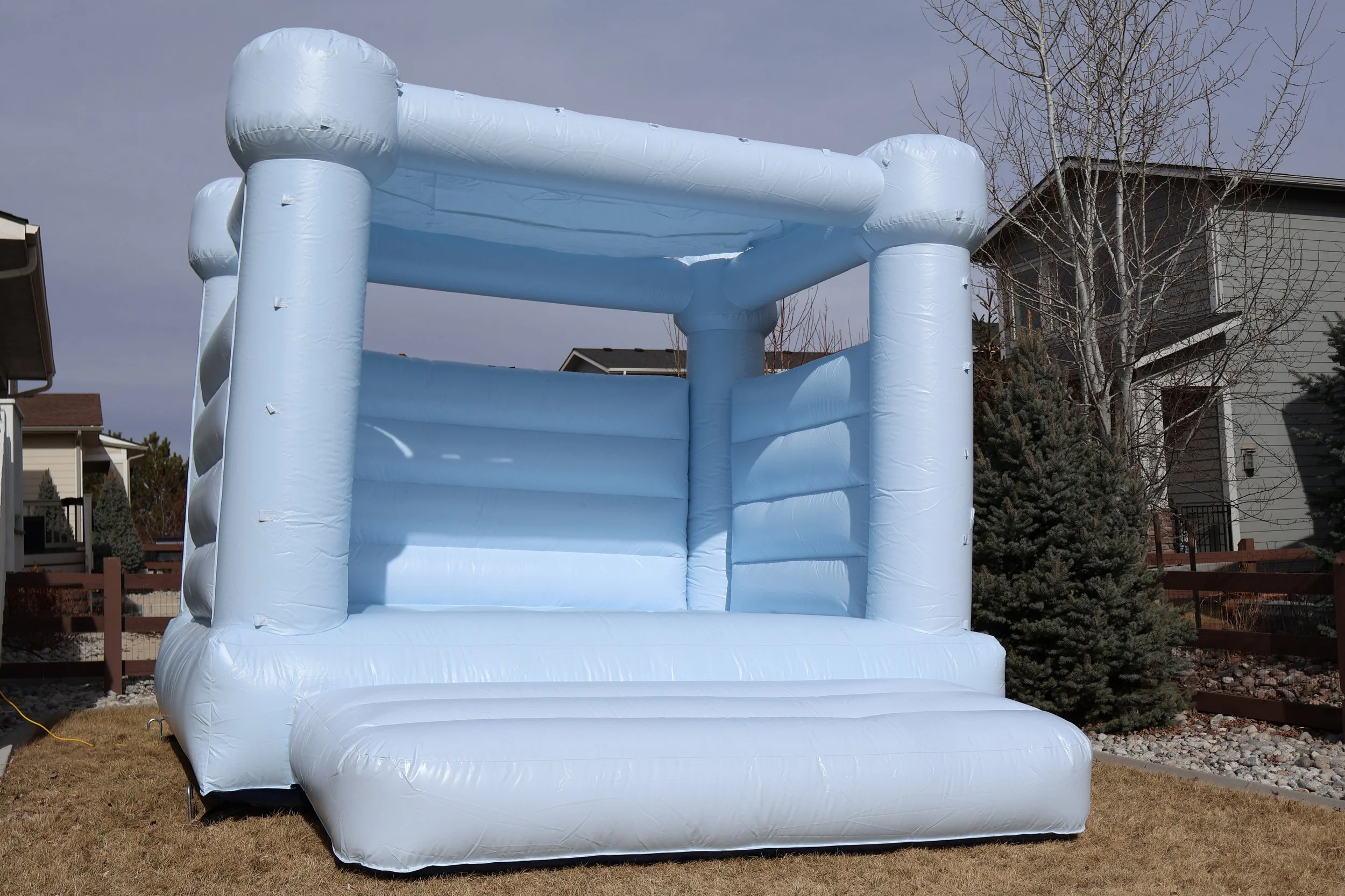Large white inflatable bounce house set up outdoors on a grassy yard with trees and houses in the background.