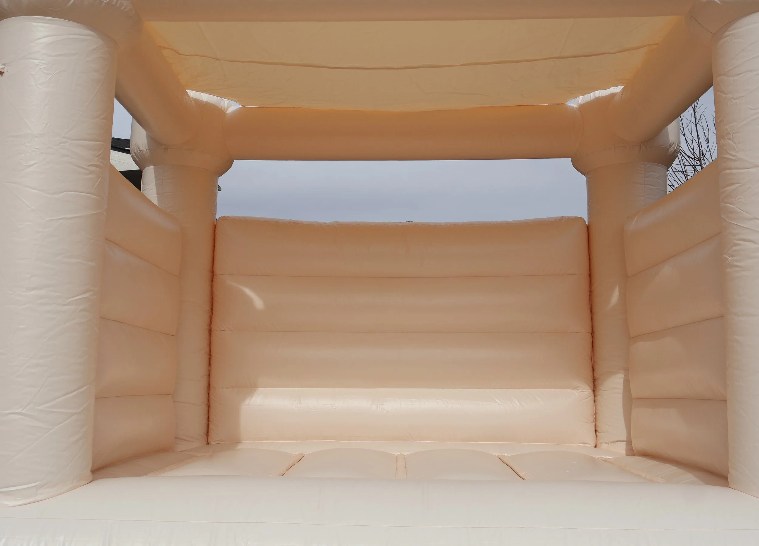 Inside view of a peach-colored inflatable bounce house with padded sides and a ceiling, view of the sky through the top opening.