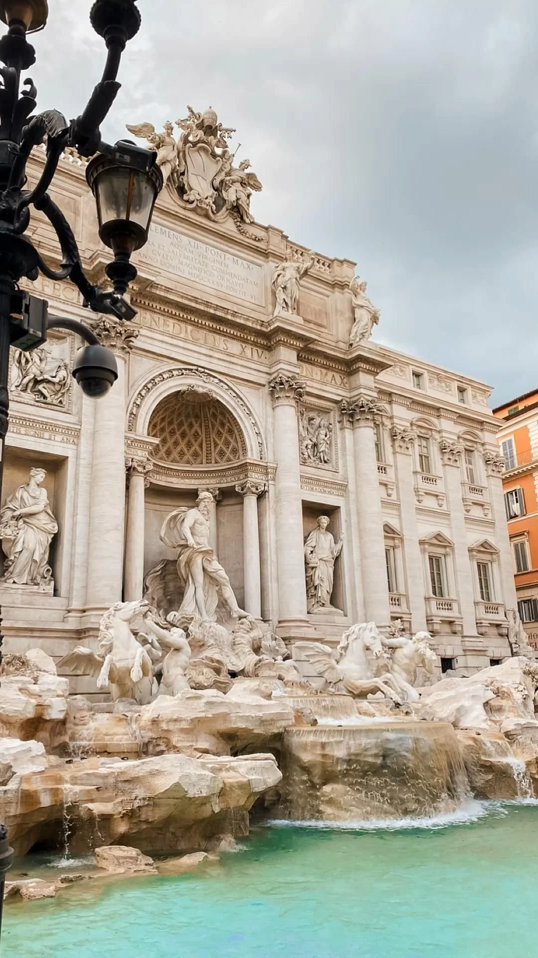 The Trevi Fountain in Rome, Italy, with sculptures of figures and horses, surrounded by buildings and a cloudy sky.