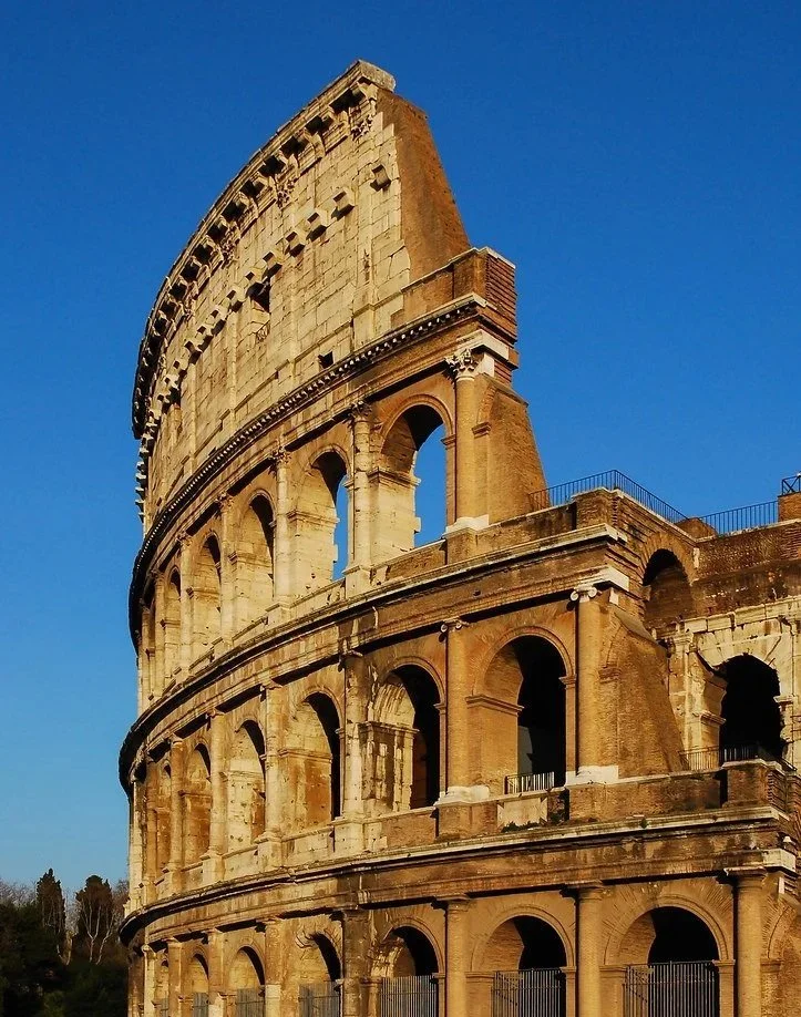 Close-up of the Roman Colosseum with arches and brickwork against a clear blue sky.