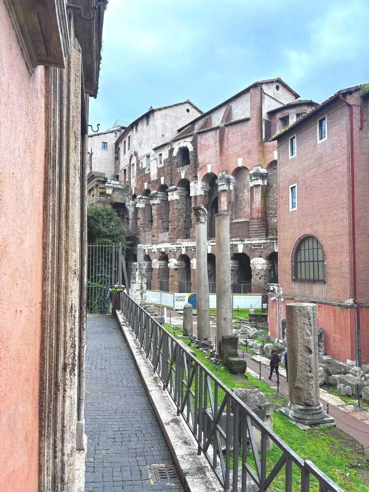 Ancient Roman ruins with standing columns and arches, adjacent to modern buildings, at an archaeological site in Rome, Italy.