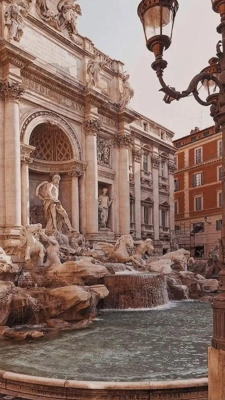 Fountain with ornate sculptures and buildings in the background, likely in Rome, Italy.