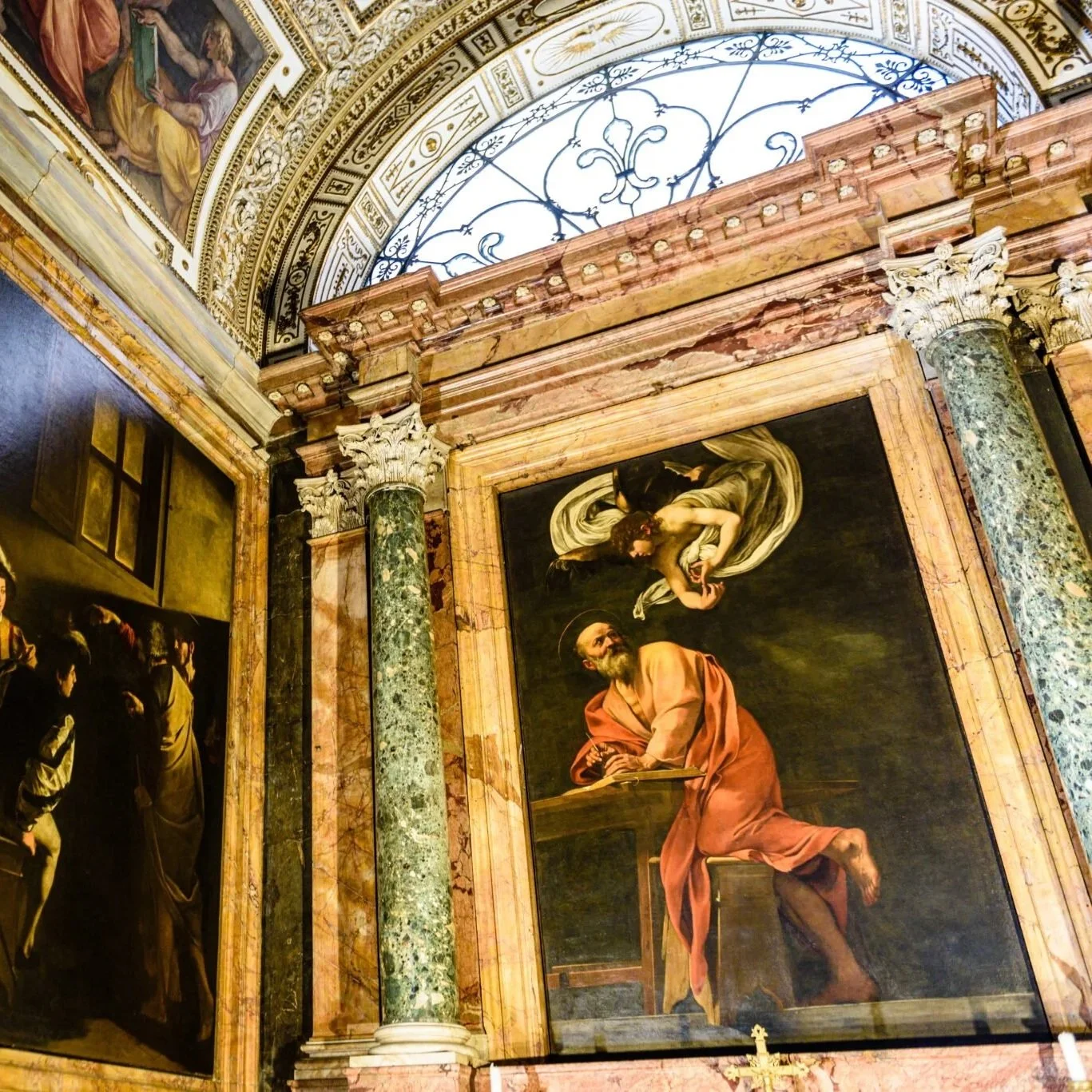 A religious painting depicting a man with a beard and long hair, wearing a pink robe, sitting at a desk, with a woman above him in a flowing dress.