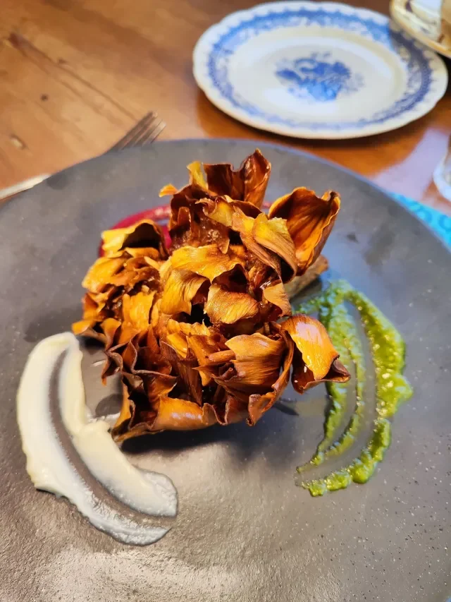Fried artichoke hearts garnished with white and green sauces on a black plate