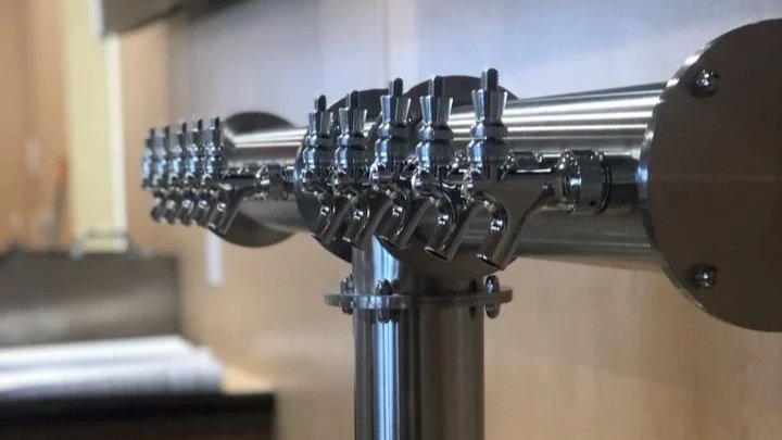 A close-up of a metallic beer tap draft system with multiple spouts in a bar or brewery setting.