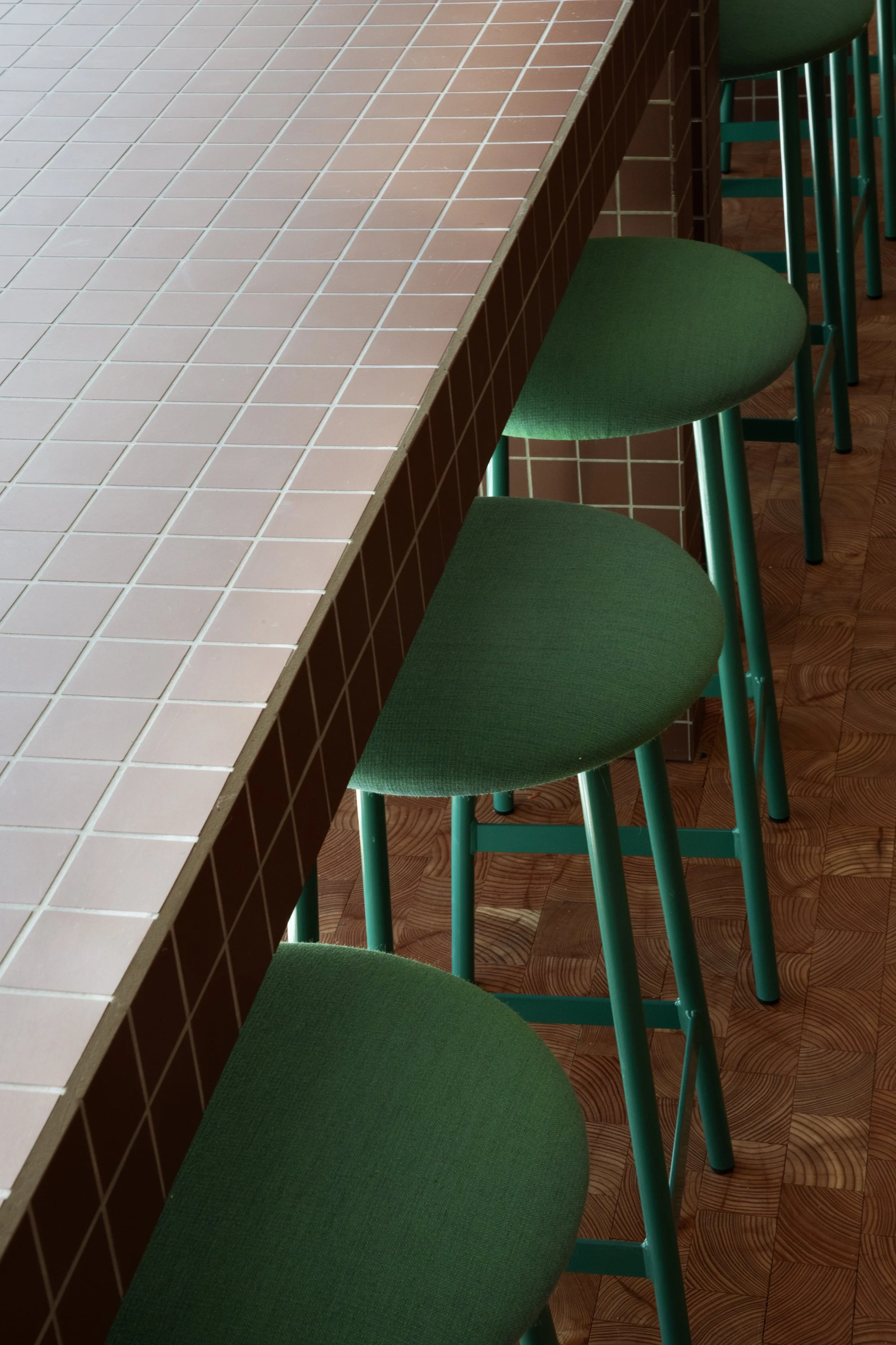A row of green bar stools with upholstered seats next to a tiled counter in a cafe or diner.