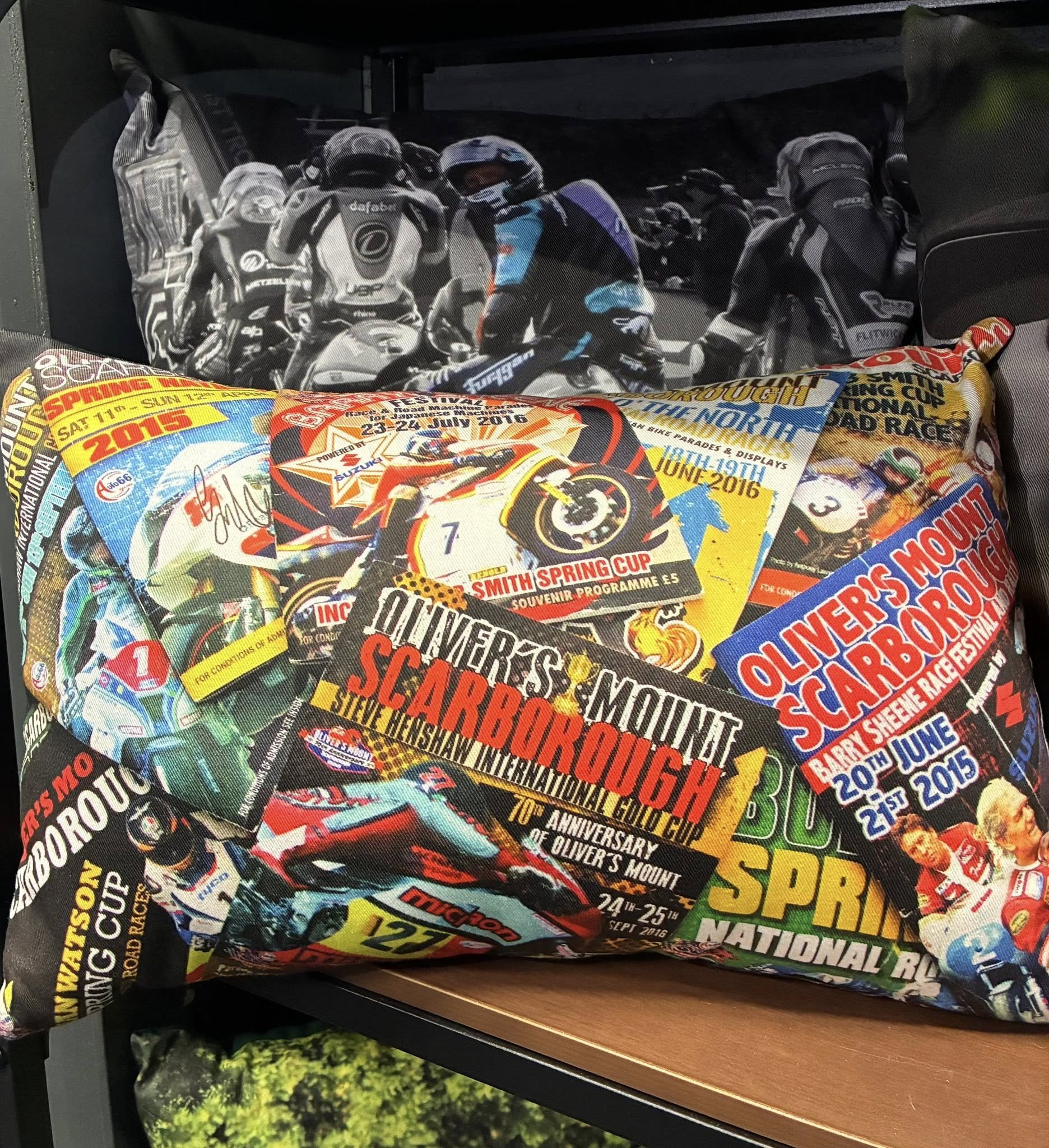 A photo of a decorative cushion featuring Oliver's Mount program covers as the design