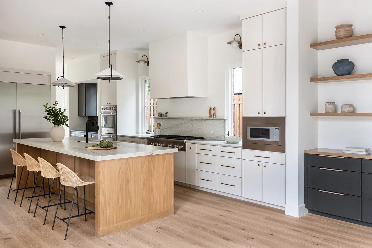 Bright modern kitchen in an Austin Northwest Hills new build featuring a natural wood island, white cabinetry, marble countertops, woven counter stools, and sculptural pendant lighting.