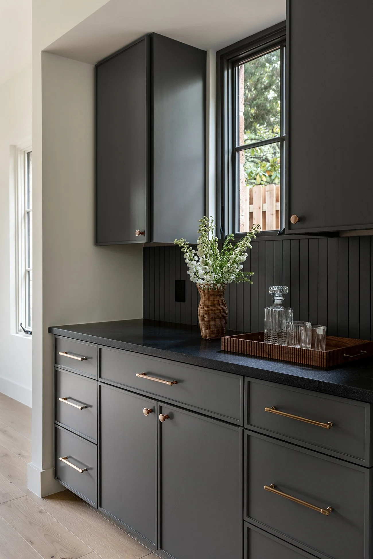 Contemporary butler’s pantry in an Austin Northwest Hills home featuring dark cabinetry, black countertops, brass hardware, vertical tile, and custom built-in storage
