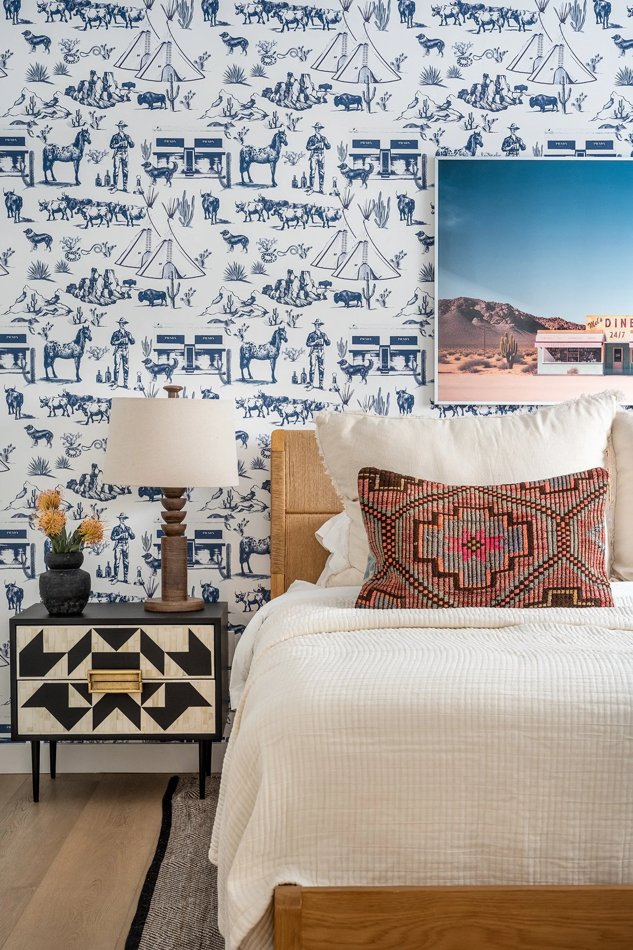 Colorful bedroom in a downtown Austin vacation rental featuring graphic blue-and-white Western toile wallpaper, layered neutral bedding, a patterned accent pillow, black-and-white furnishings, and playful Texas-inspired details that continue the dupl
