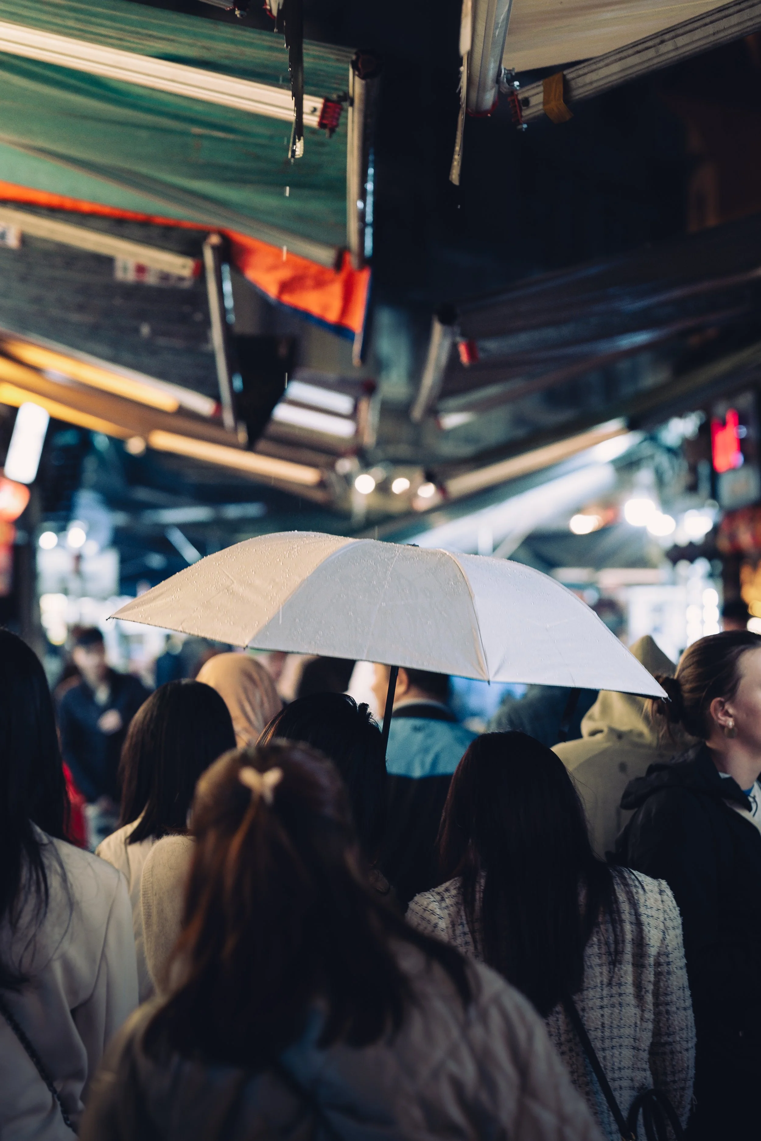 Crowded street scene at night with people holding umbrellas, illuminated by city lights.