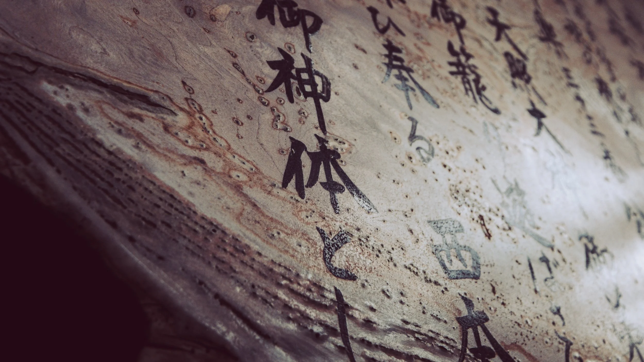 Close-up of an ancient manuscript with Chinese calligraphy, showing ink characters on aged, textured paper.