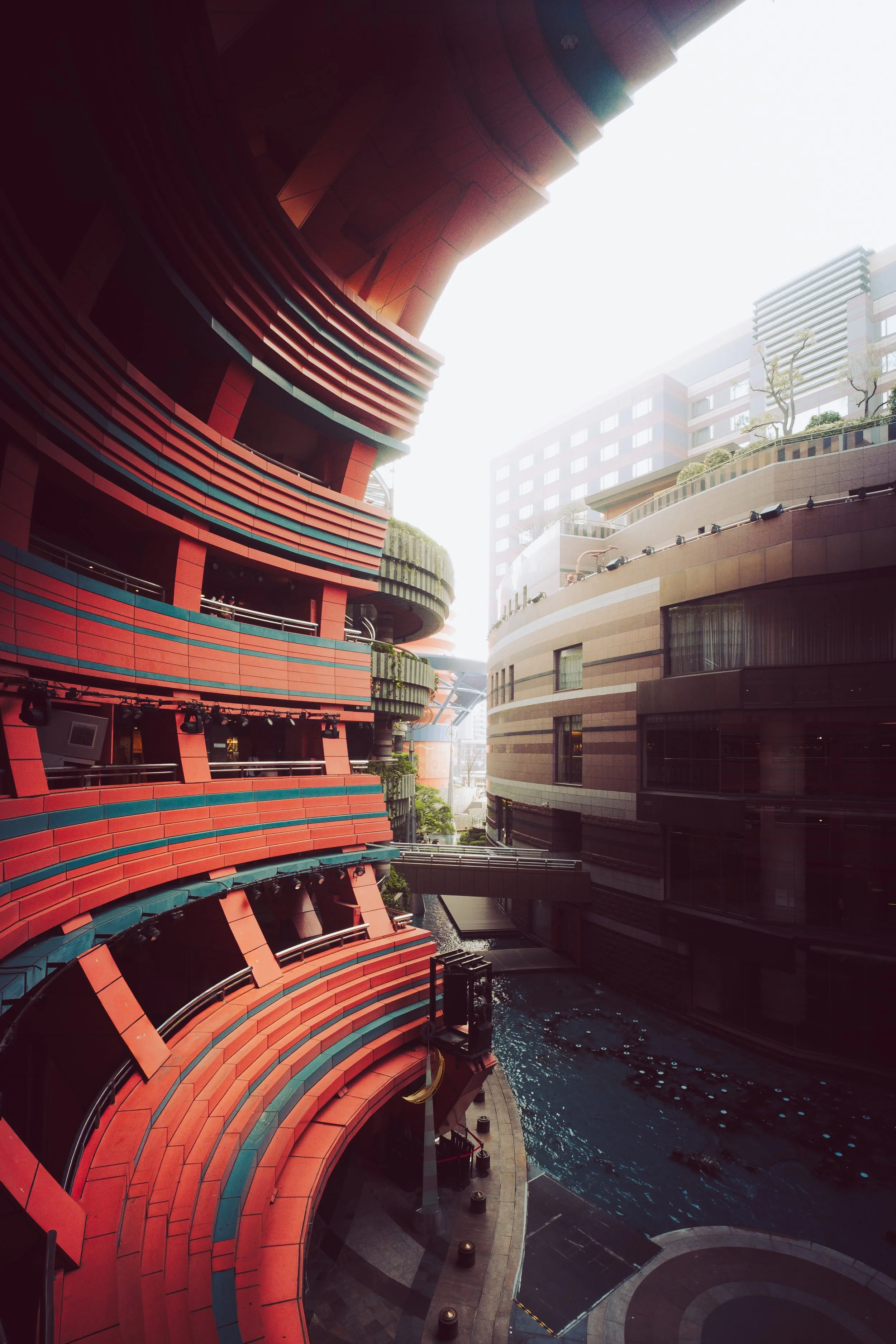 Modern urban buildings with curved balconies, glass windows, and a water feature in a cityscape.