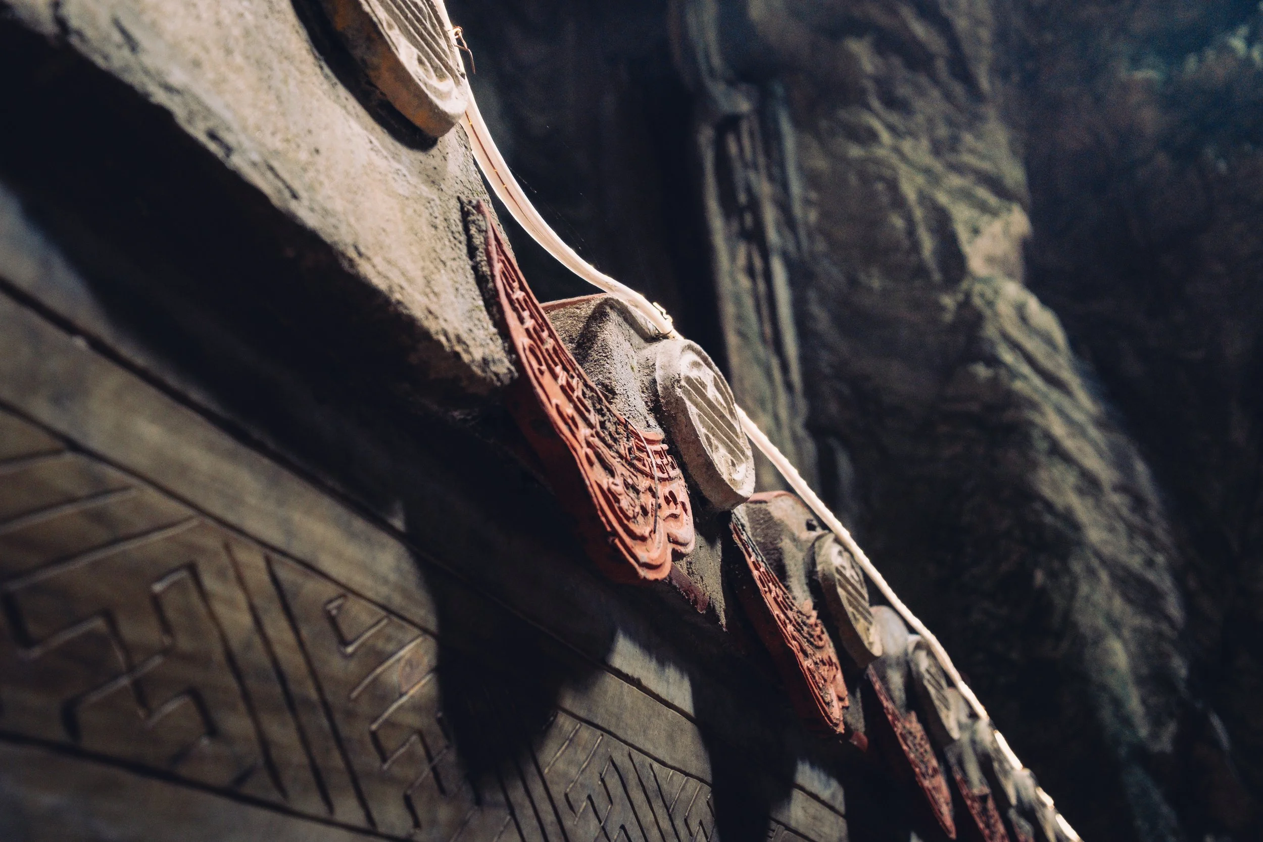 Close-up of traditional Asian roof tiles with carved decorations, mounted along a wooden beam with a dark stone or brick background.