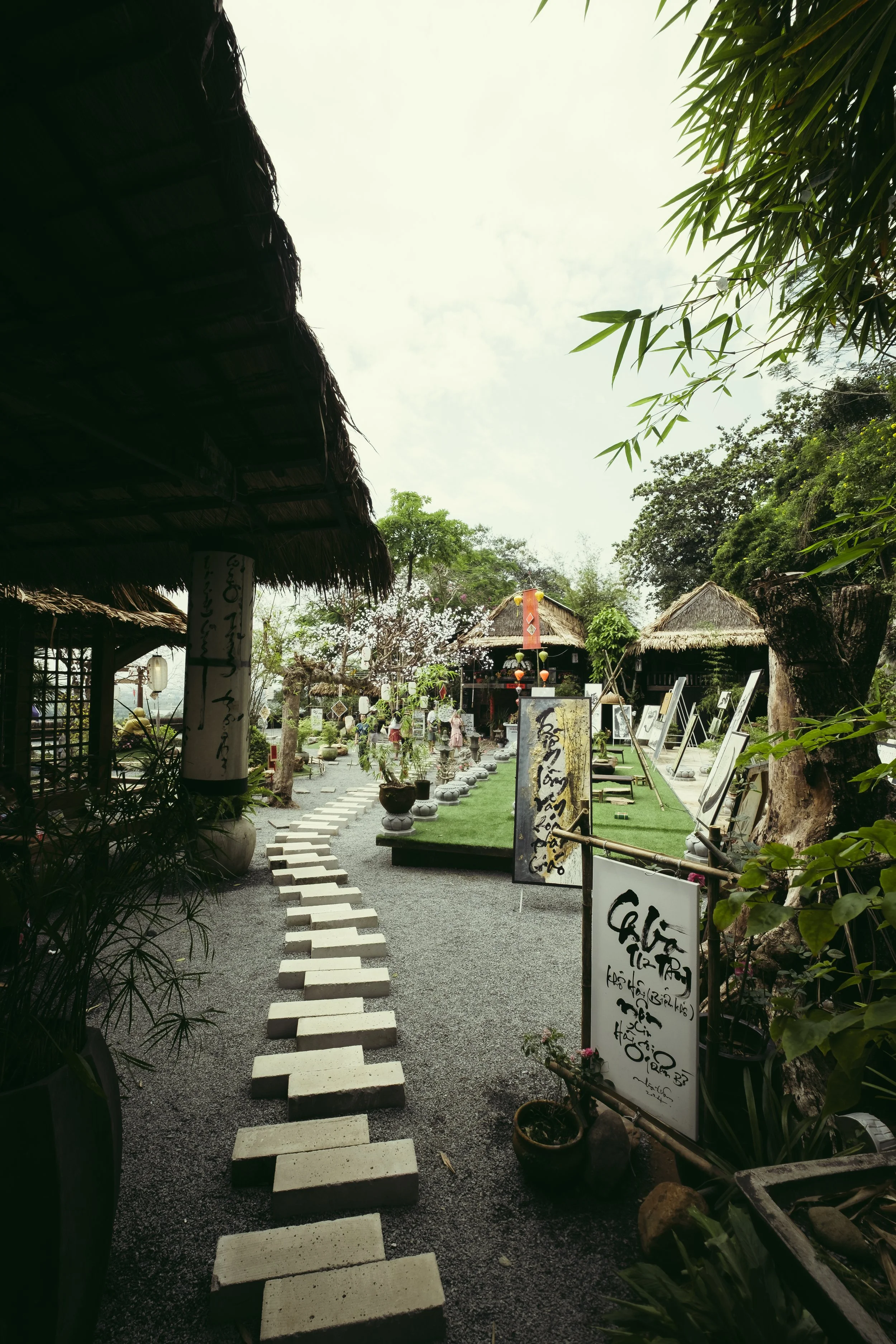 Pathway with stepping stones leading to outdoor art gallery surrounded by trees and traditional style structures.