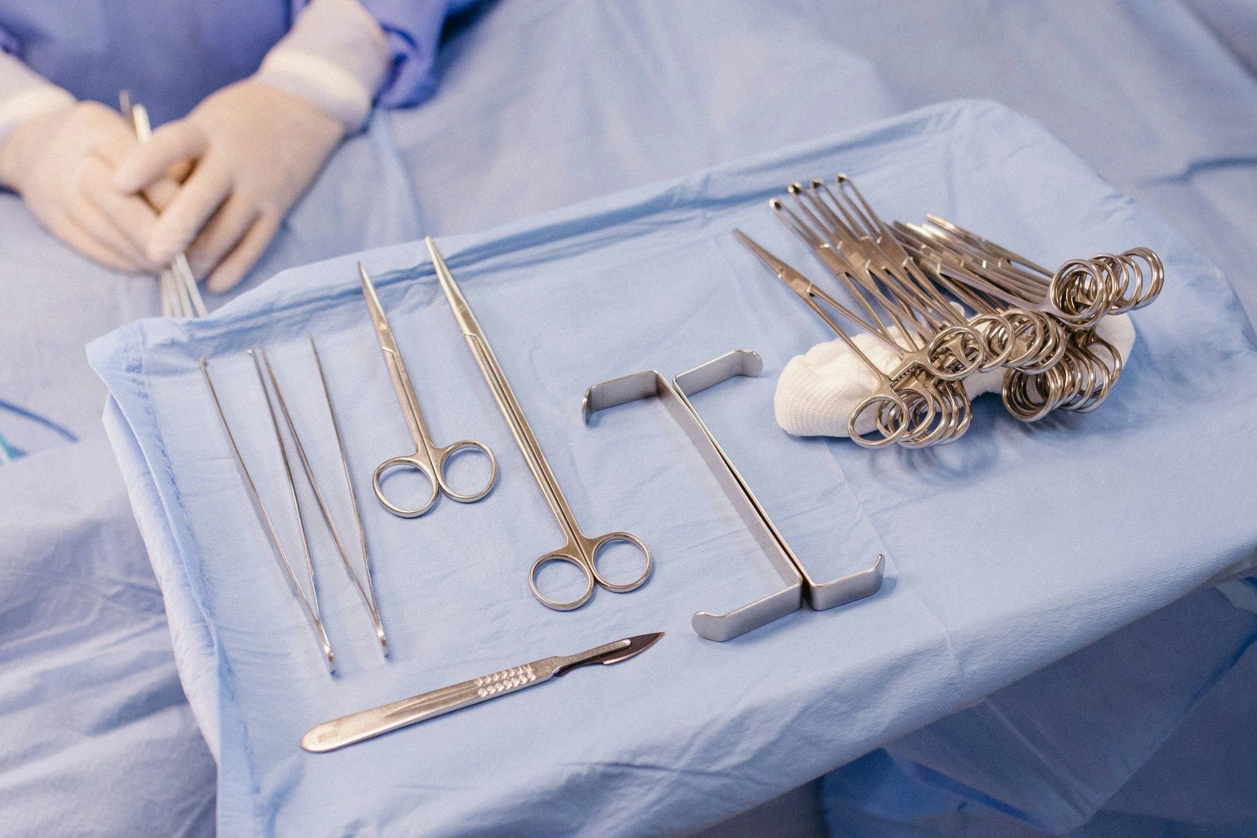 A sterile medical surgical tray with surgical instruments such as scissors, forceps, scalpels, and retractors, with a gloved hand visible in the background.